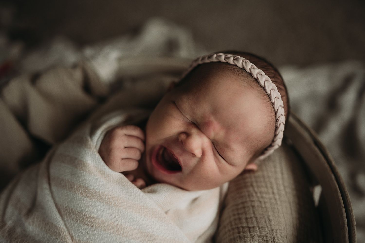 Side view of infant in white wrap expressing emotion against textured background.