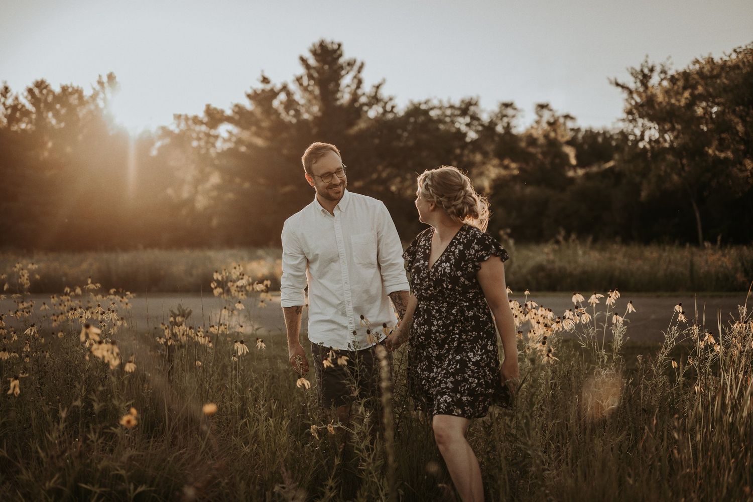 Couple walking together through tall grass and wildflowers at sunset.