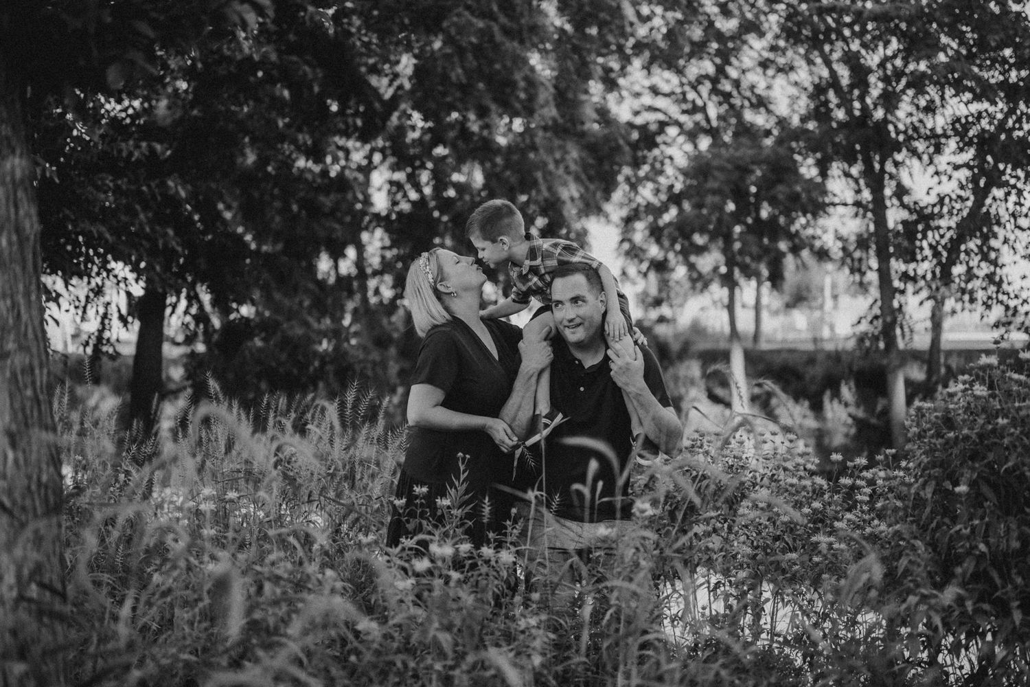 Black and white portrait of a family enjoying a moment together in a wildflower meadow at sunset.