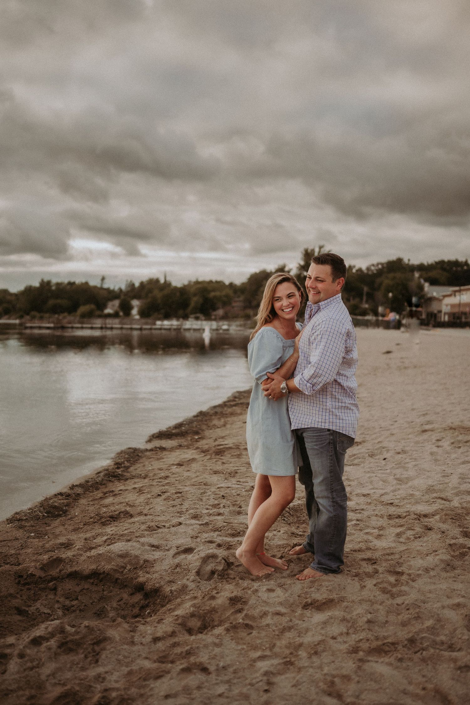 A joyful couple embraces on a sandy beach with dramatic stormy skies.