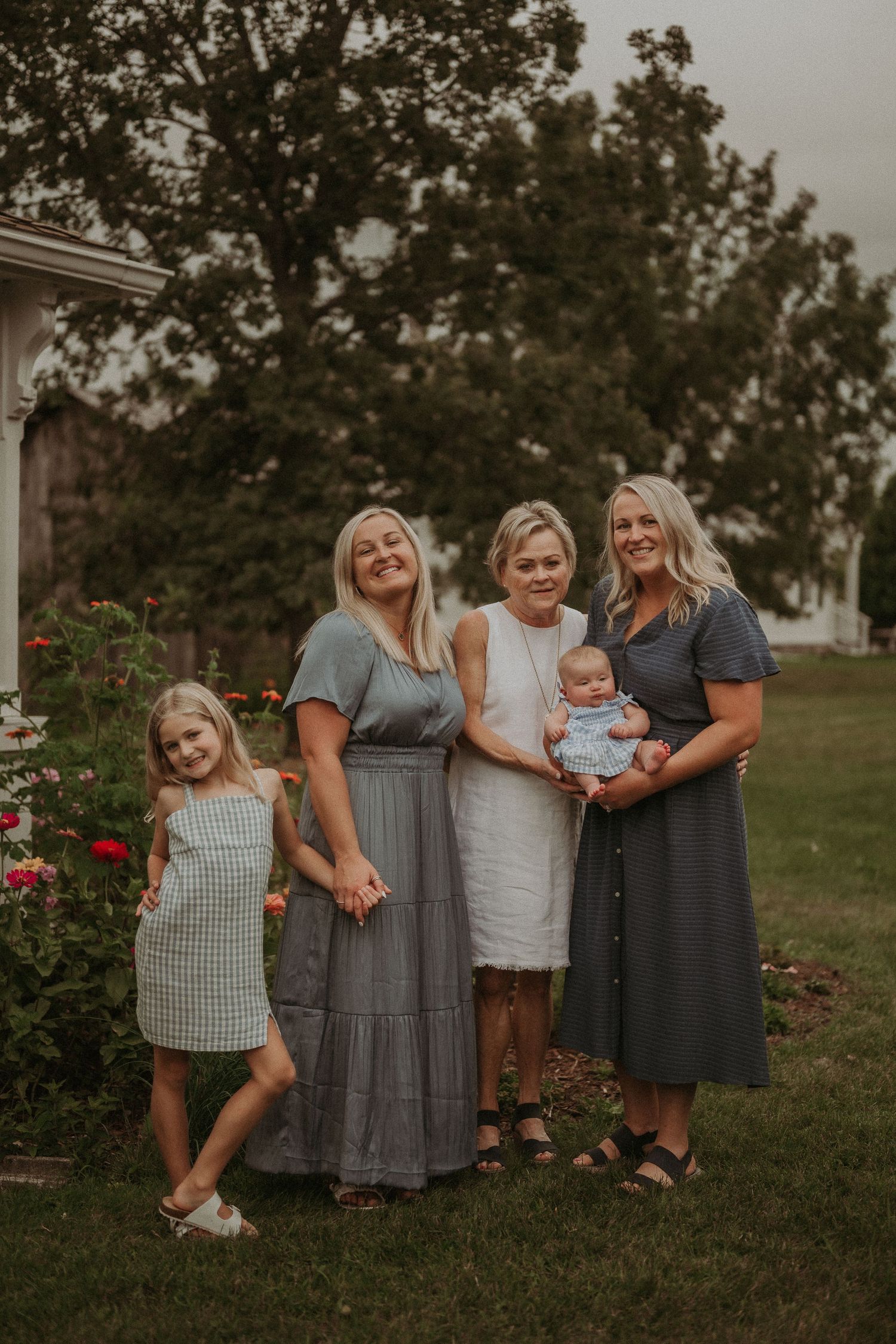 Multi-generational family portrait in a garden setting with roses and trees in warm evening light.