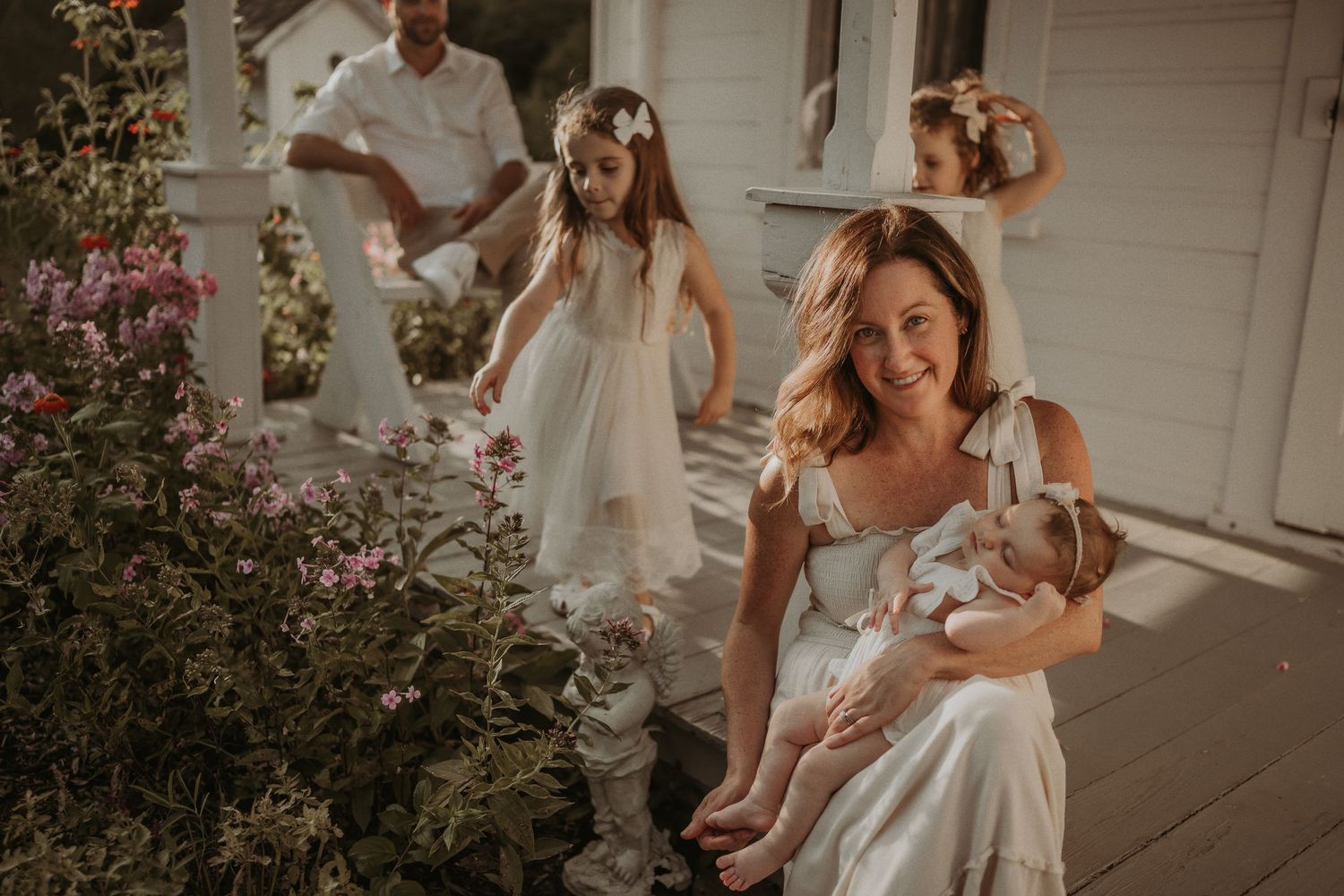 A dreamy sunset photoshoot on a white porch with flowering bushes in the foreground.