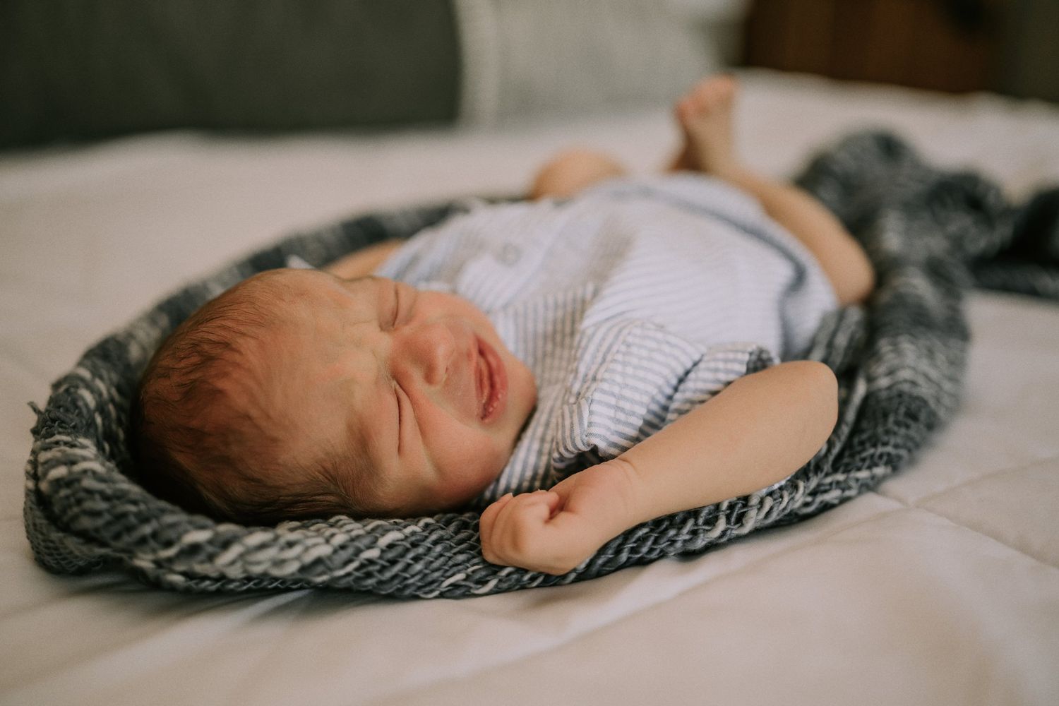 Close-up of peaceful sleeping infant wearing white outfit on textured gray blanket.