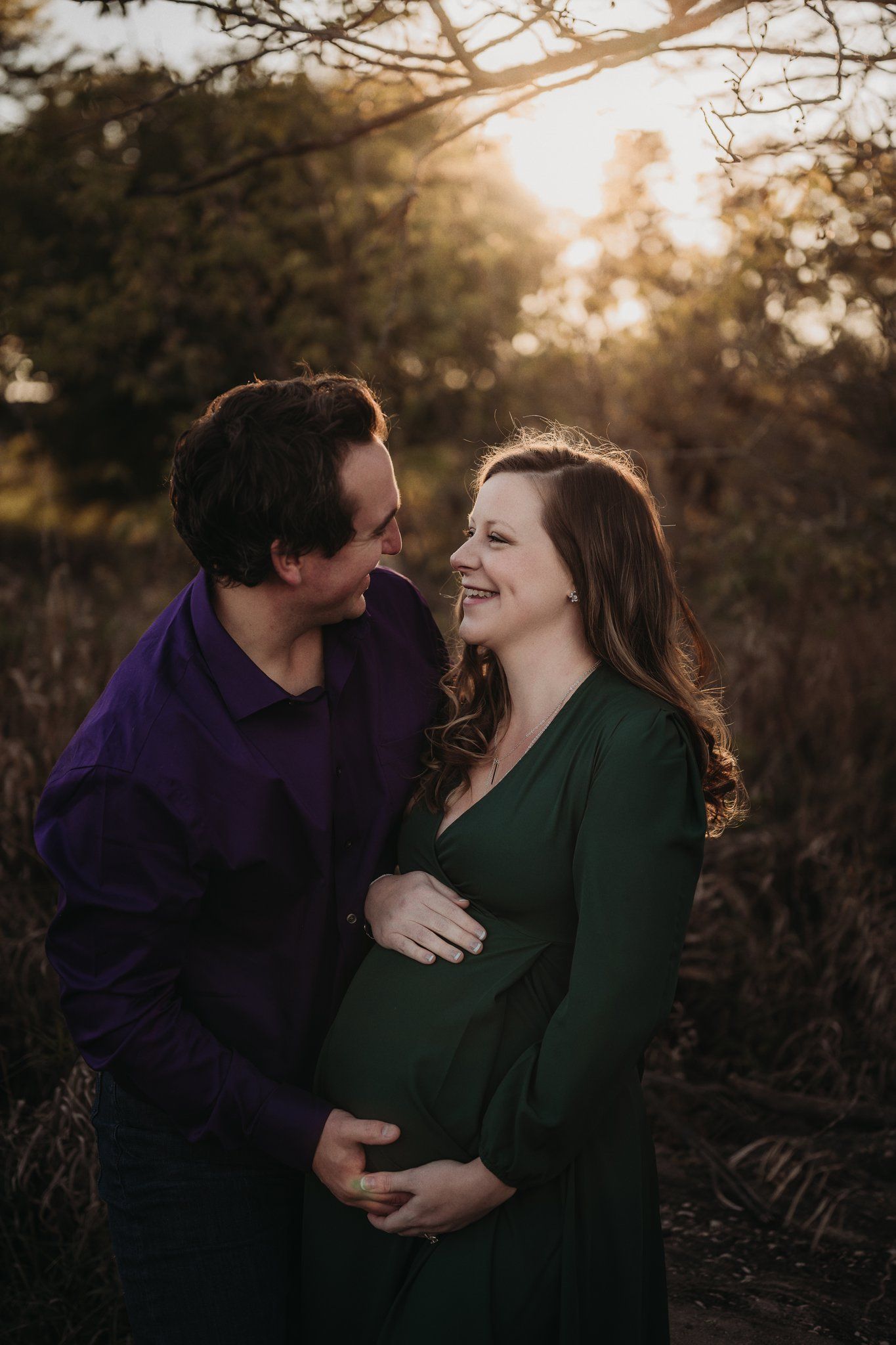 A joyful maternity portrait of a couple laughing together in warm sunset light.