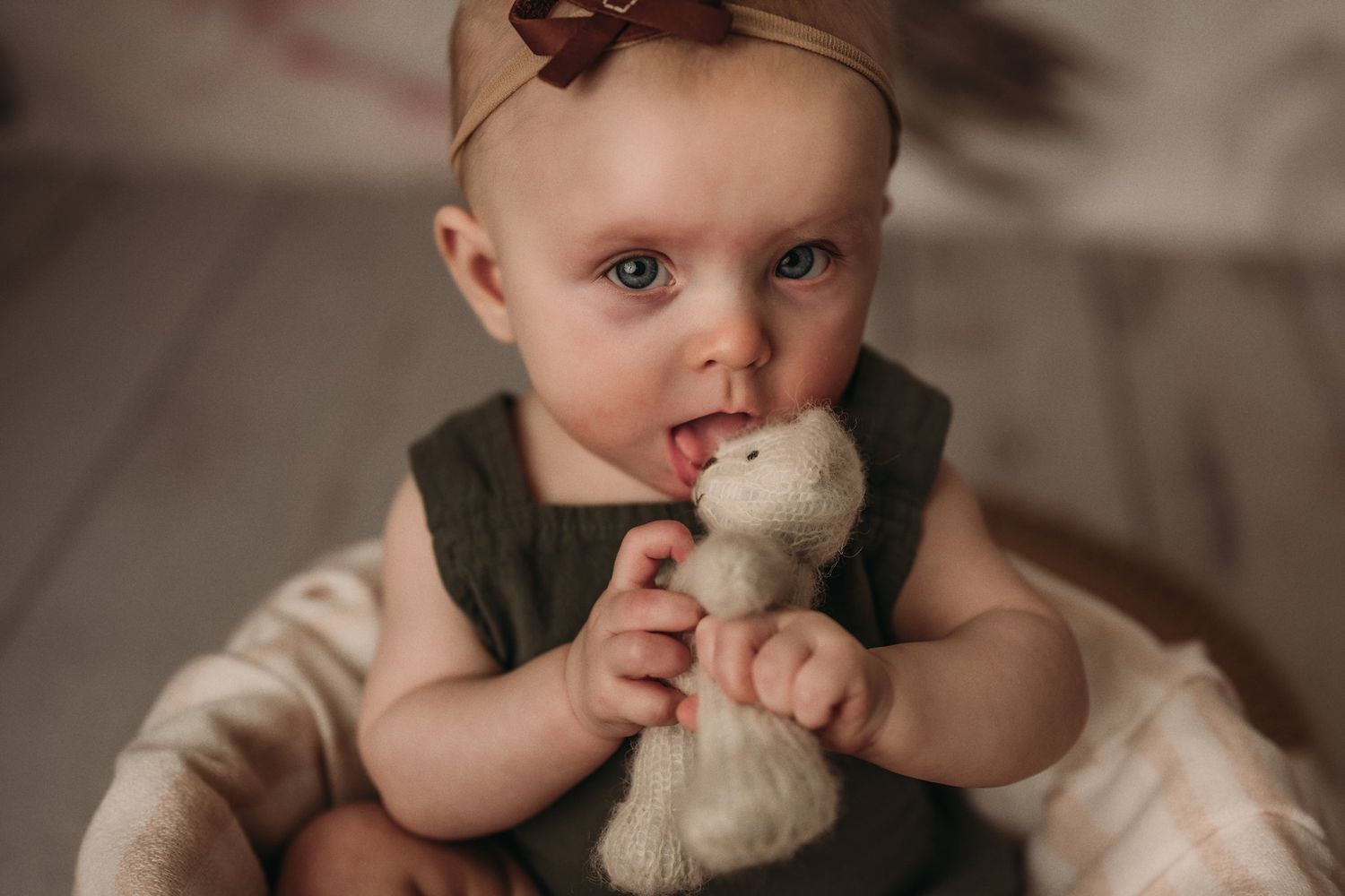 Young child in green outfit holding and chewing on a small white plush toy.