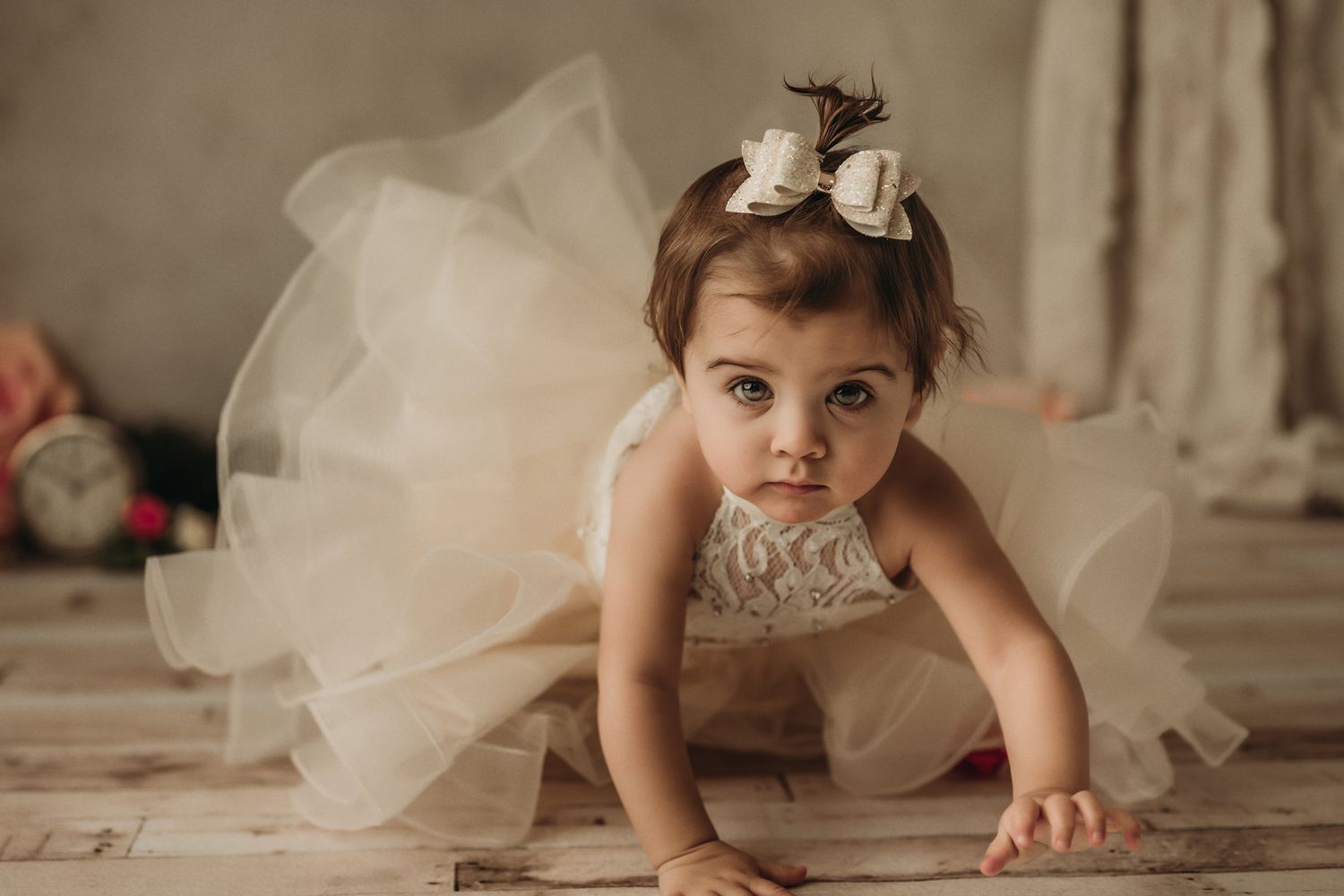 A dreamy portrait captures movement in cream tulle dress against wooden flooring.