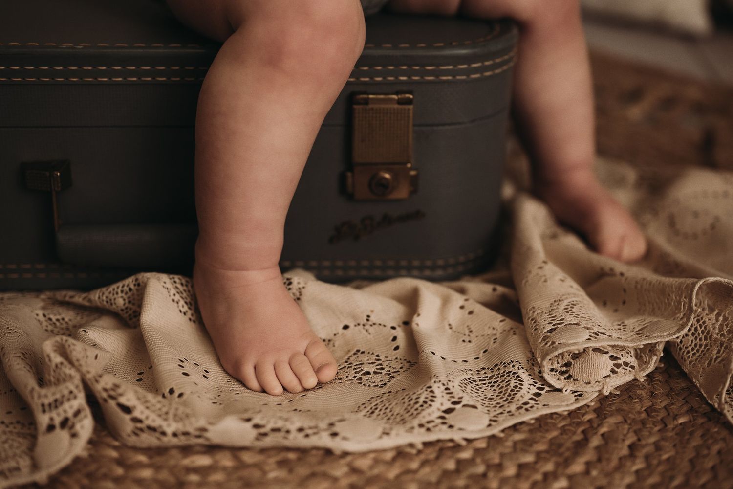 Tiny bare feet standing on vintage lace fabric next to an old leather suitcase.