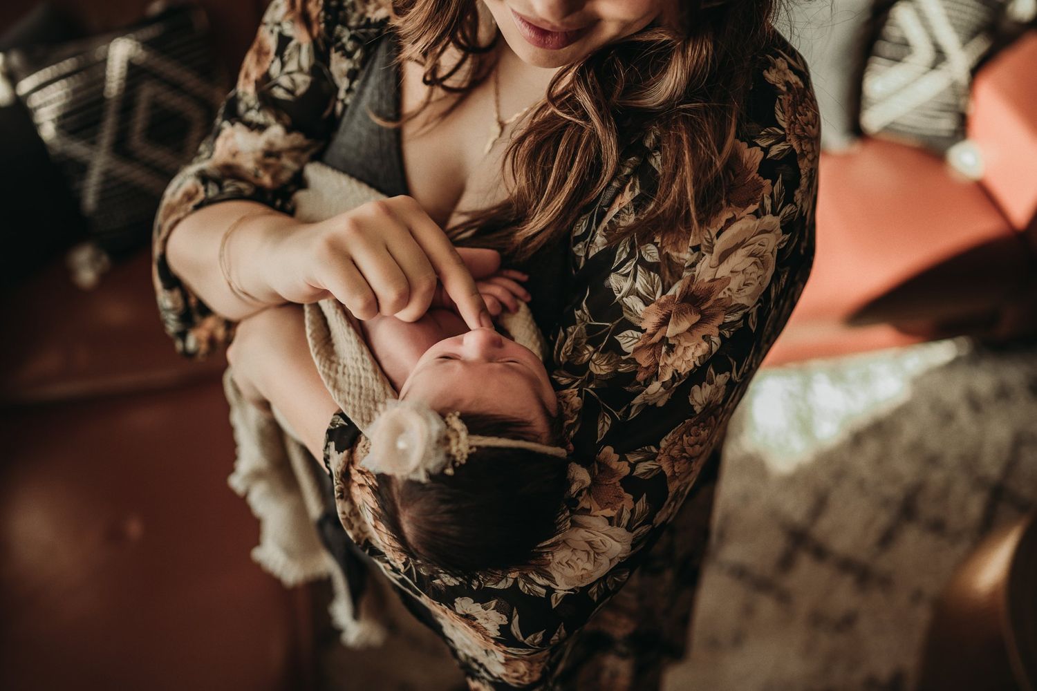A tender moment between parent and baby in a floral dress against warm lighting.