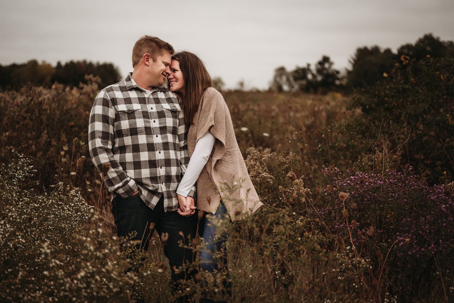 A romantic fall outdoor portrait of a couple embracing in a field of wildflowers at sunset.