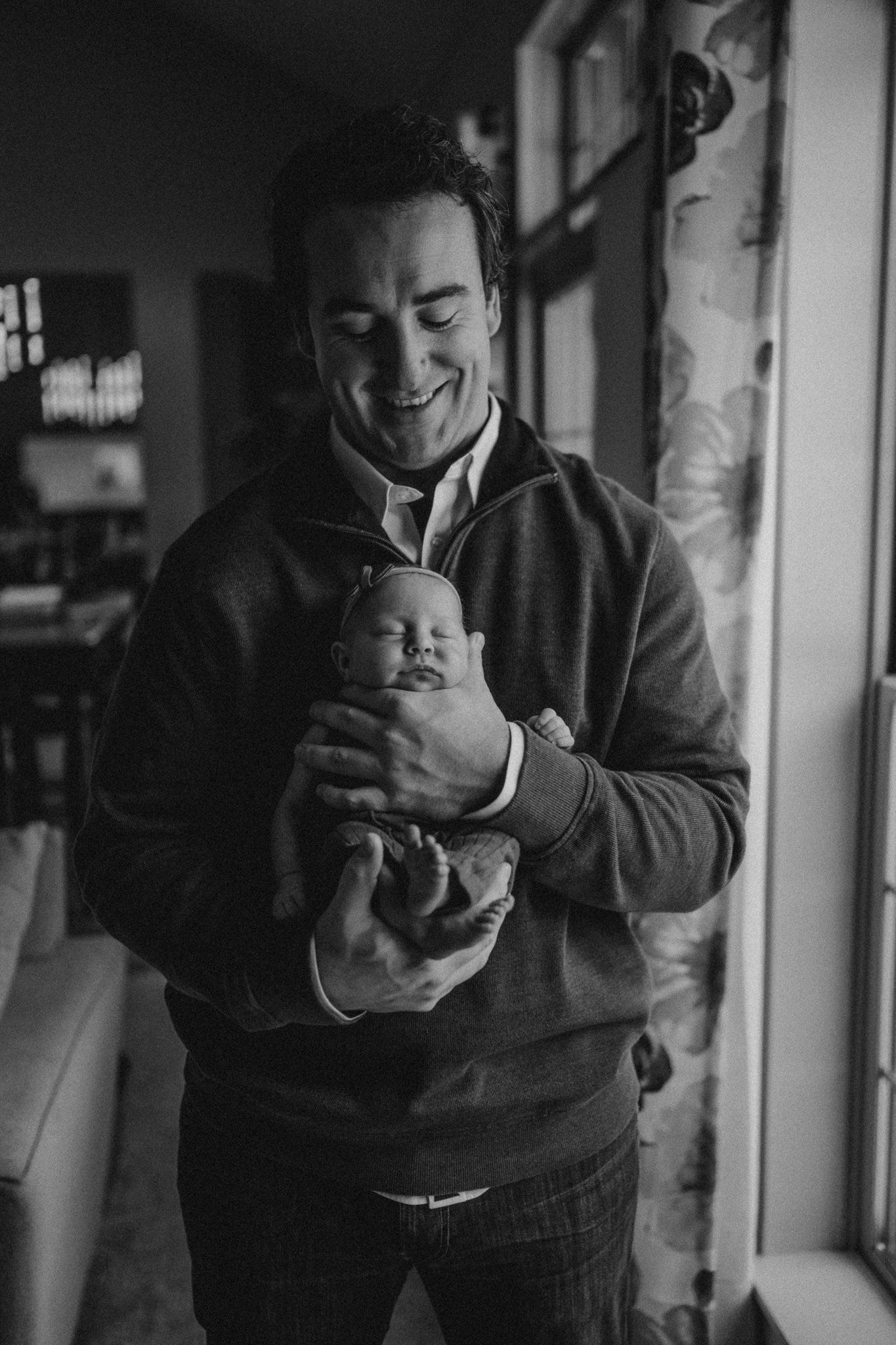 Joyful moment with newborn baby by window in black and white photography.