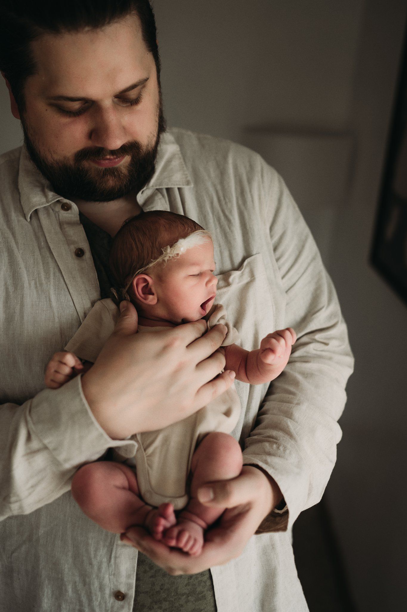 A person in a light button-up shirt tenderly holds a sleeping newborn baby.