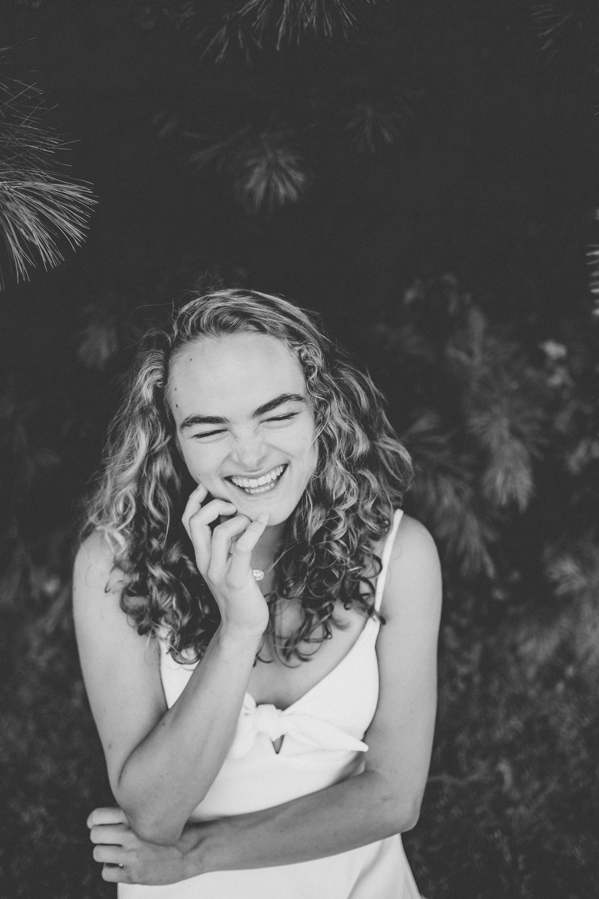 Black and white candid shot capturing genuine laughter against pine branches.