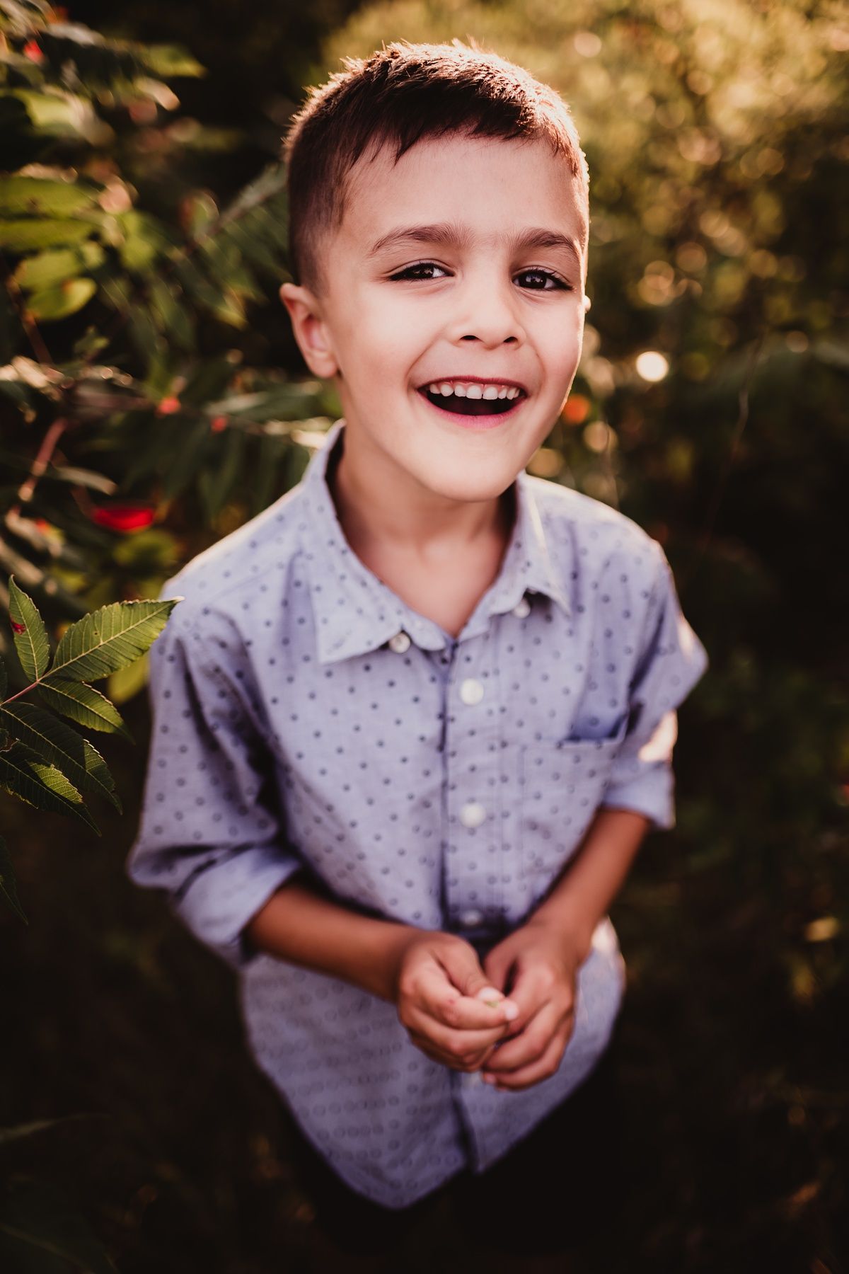Close up portrait of child in dotted shirt laughing joyfully in garden setting.