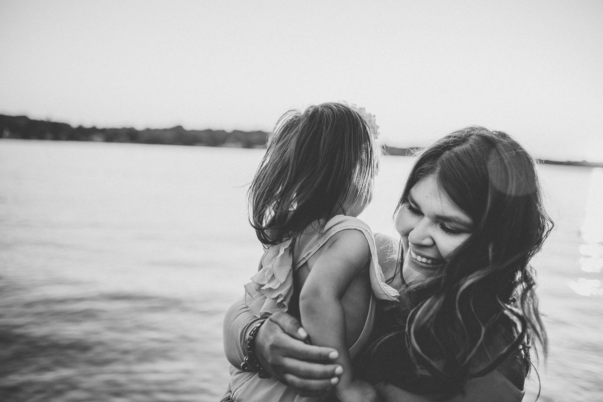 A touching black and white lakeside moment between child and adult playing together at sunset.