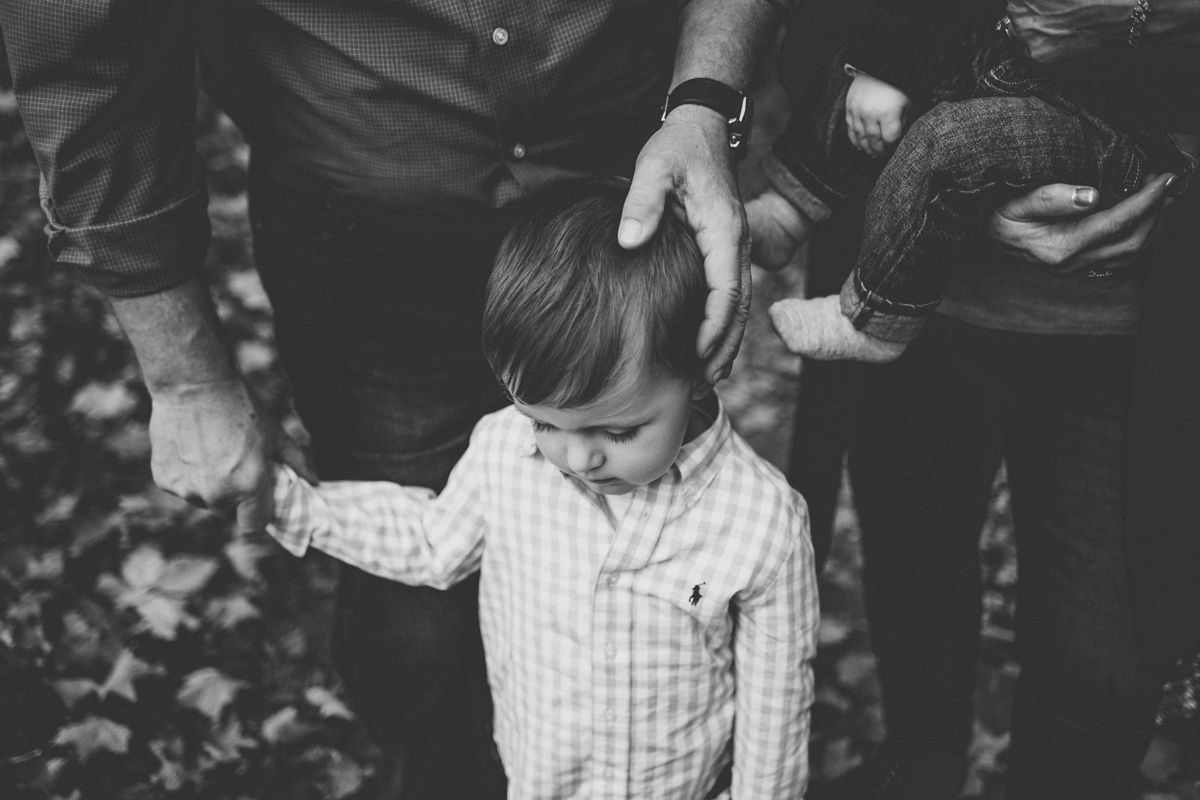 Black and white photo of small child in plaid shirt holding hands with adults.