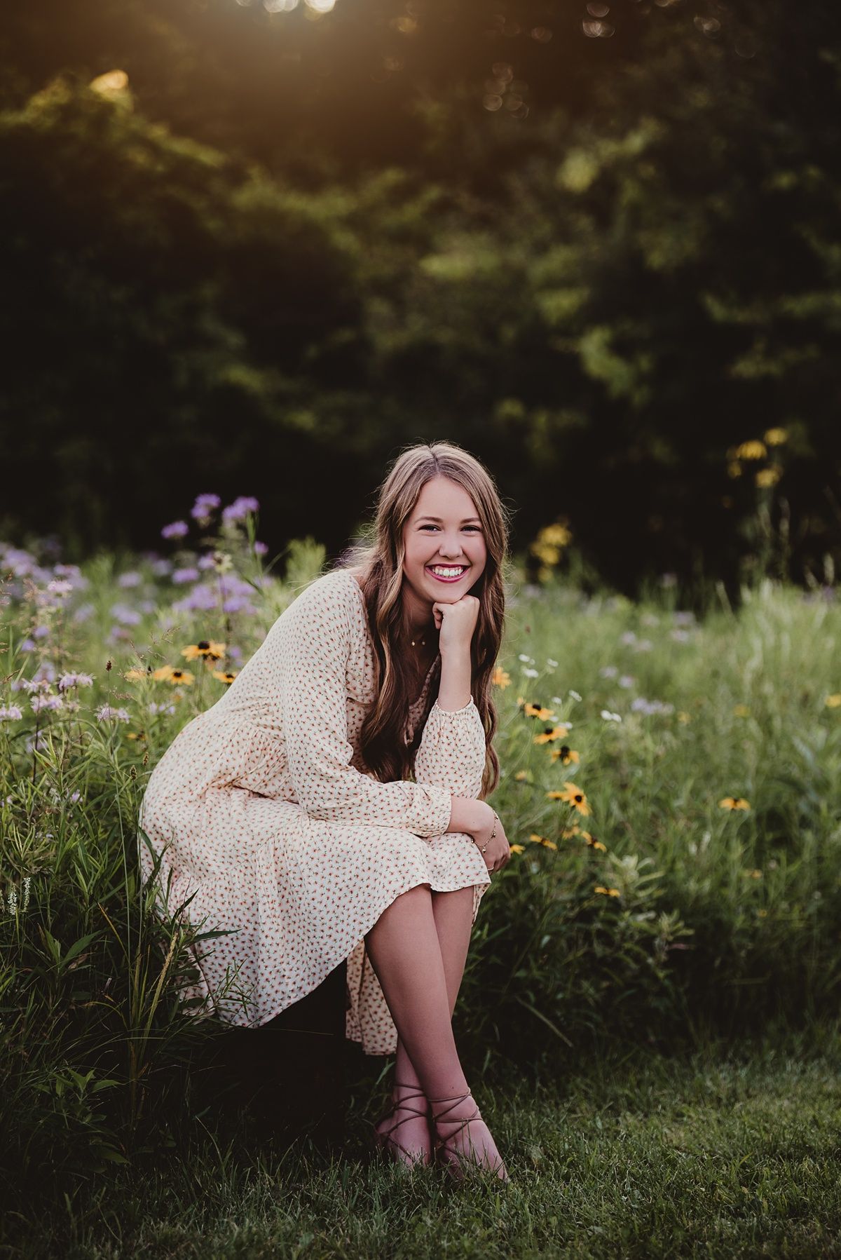 Portrait in a wildflower meadow wearing cream dress while sitting on grass at sunset.