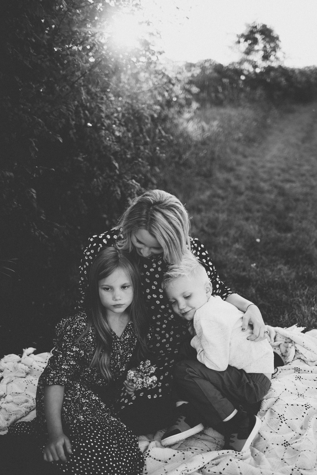 Black and white portrait of family gathering on picnic blanket outdoors.