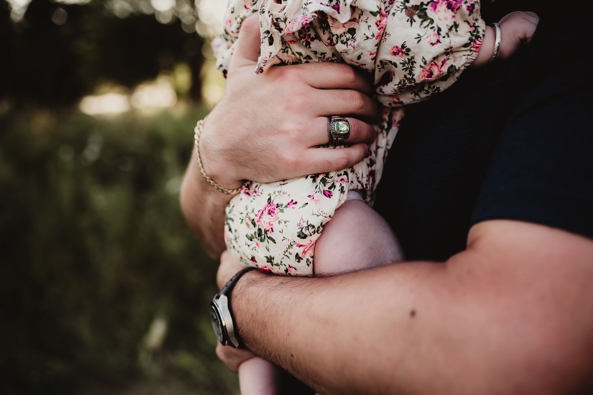 Close-up of hands holding baby wearing floral outfit in outdoor setting.