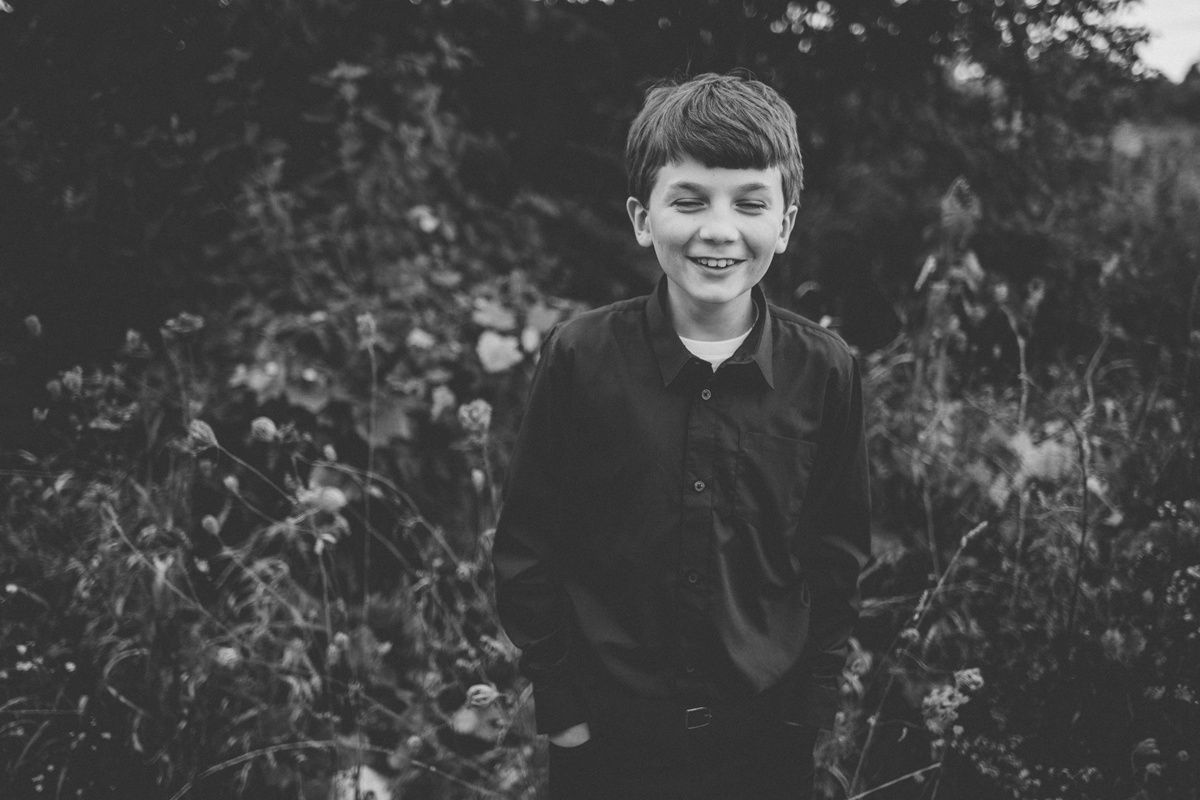 A black and white portrait of a young person in formal wear smiling in a garden setting.