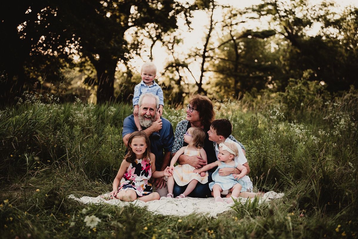 Family sitting together on a blanket in a grassy field during golden hour sunset.