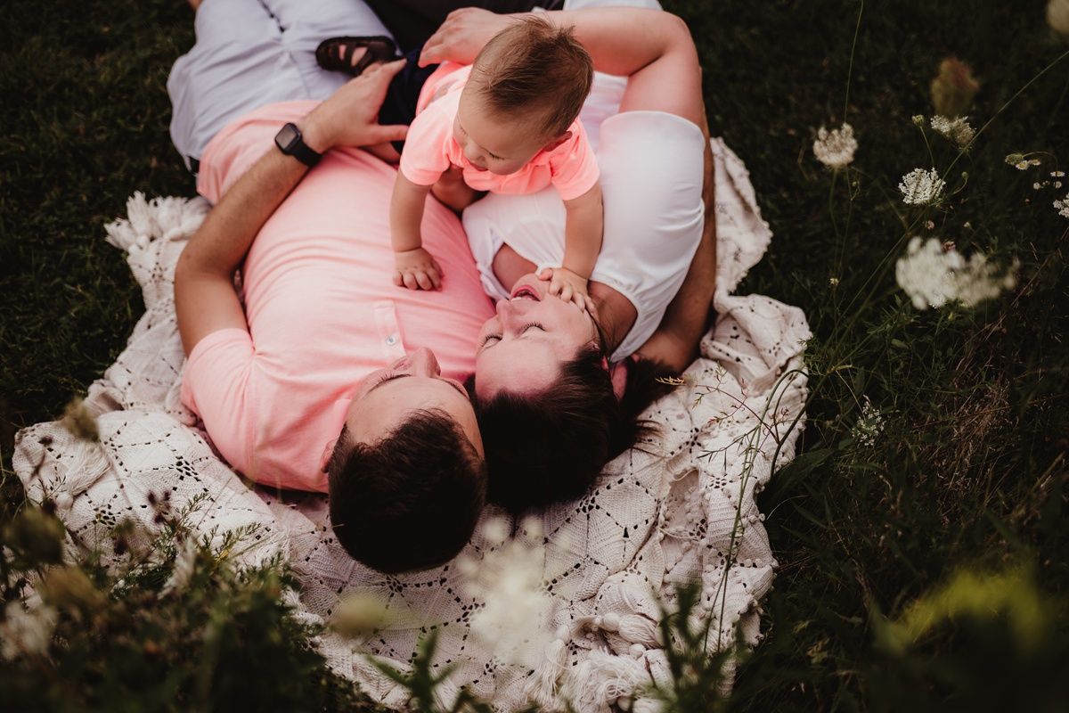 Intimate overhead view of parent and baby lying on white blanket surrounded by flowers.