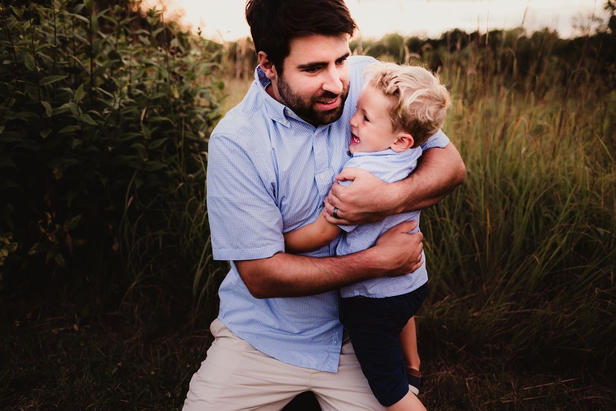 Playful embrace captured during outdoor family photoshoot in tall grass at sunset.