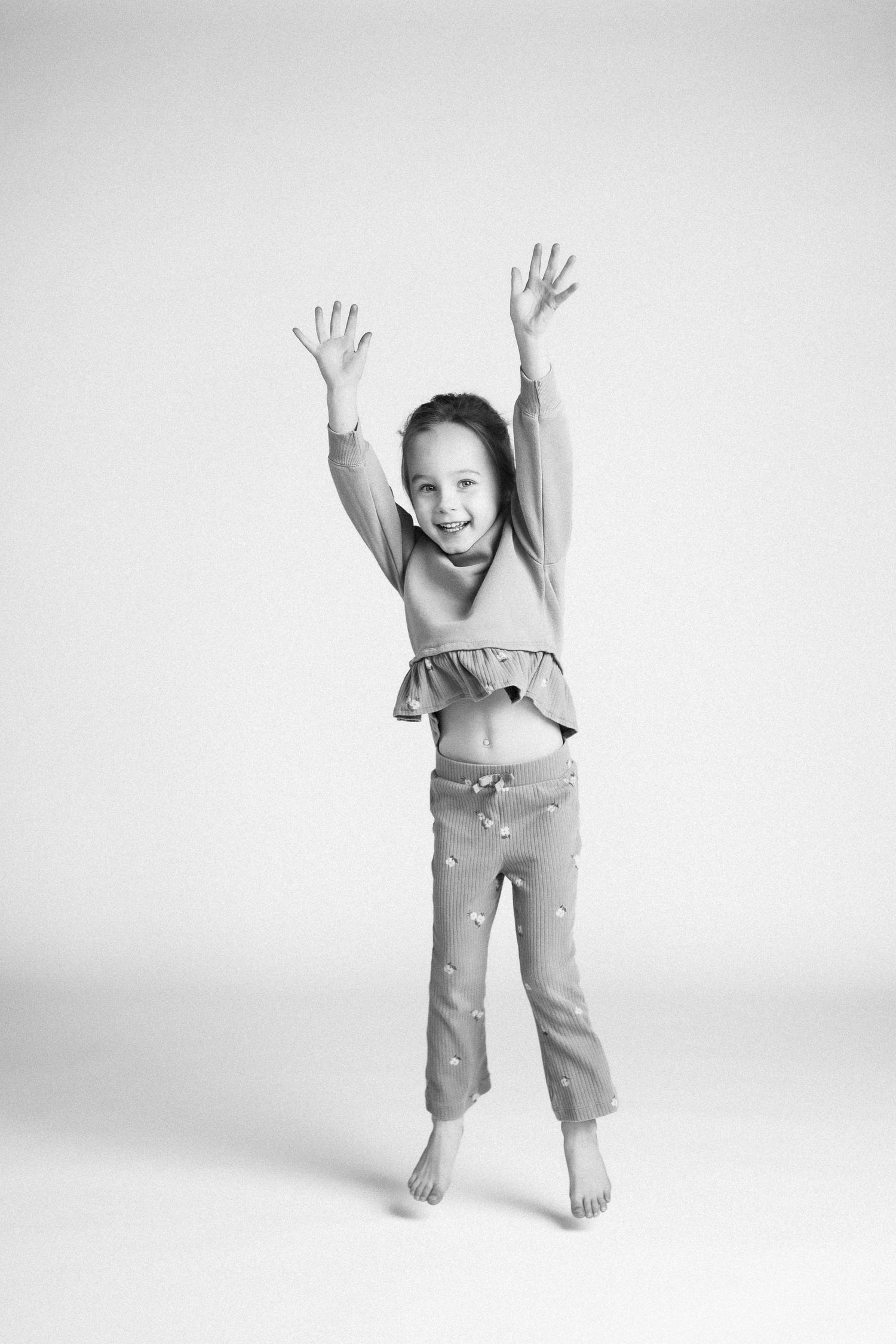 Black and white photos of a playful child jumping and posing with raised arms against a white backdrop.