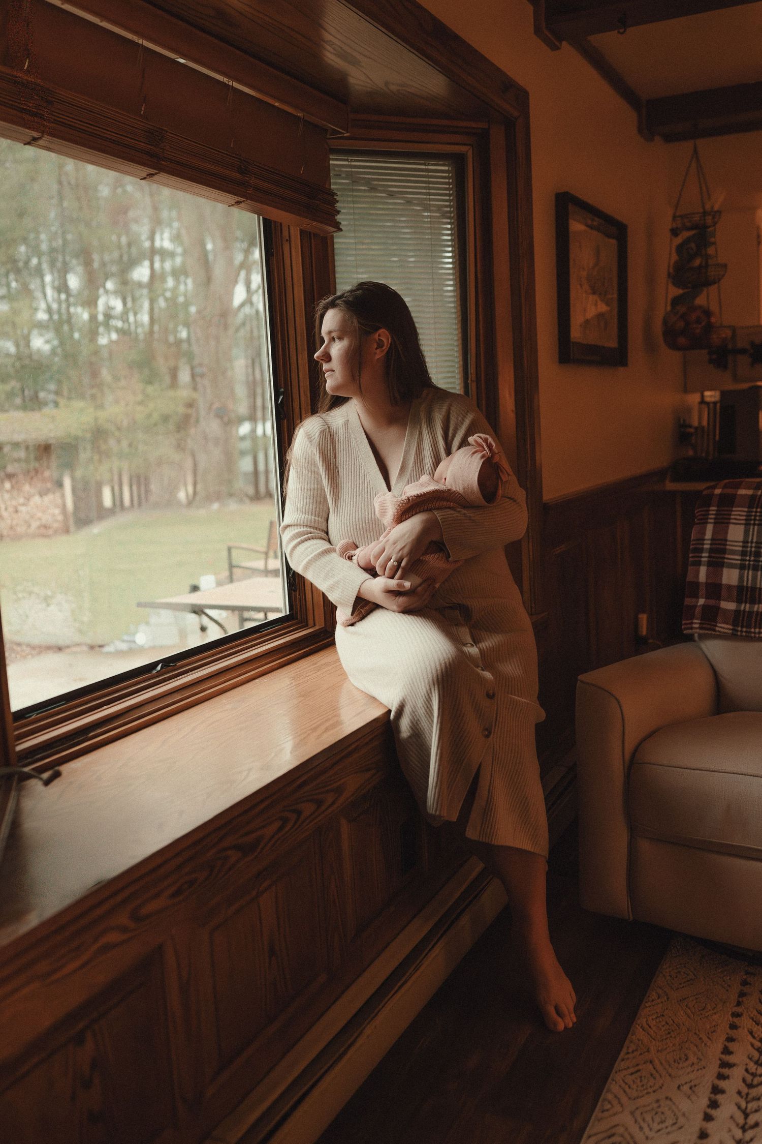 Silhouette of a person in white standing by large windows overlooking a wooded landscape.
