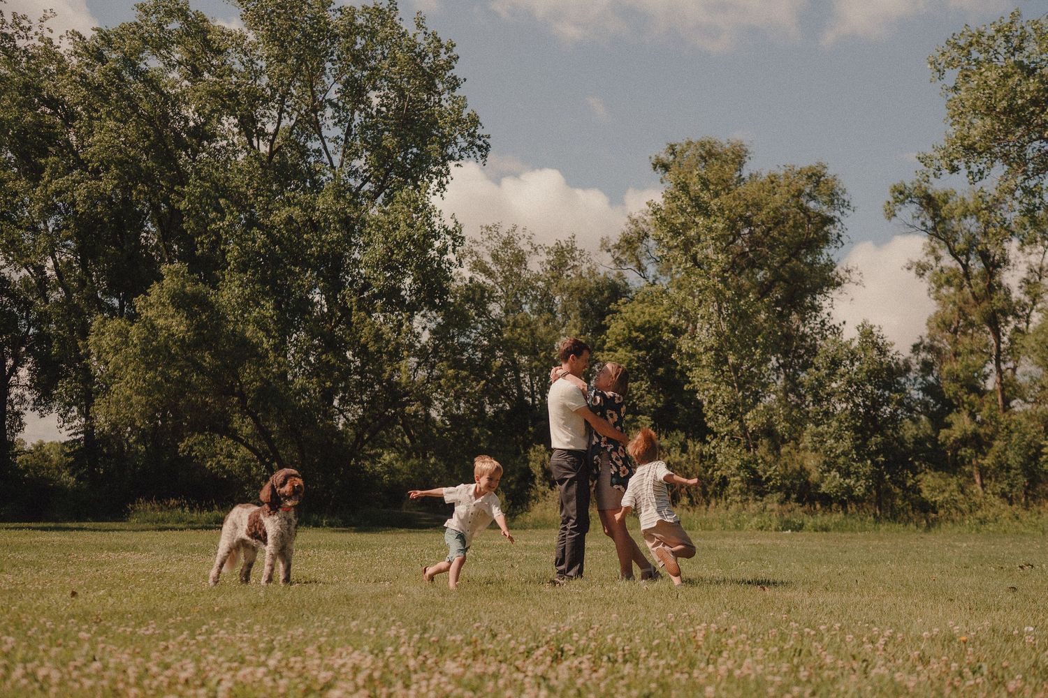 Family with dog playing together on a green lawn with trees in the background on a sunny day.