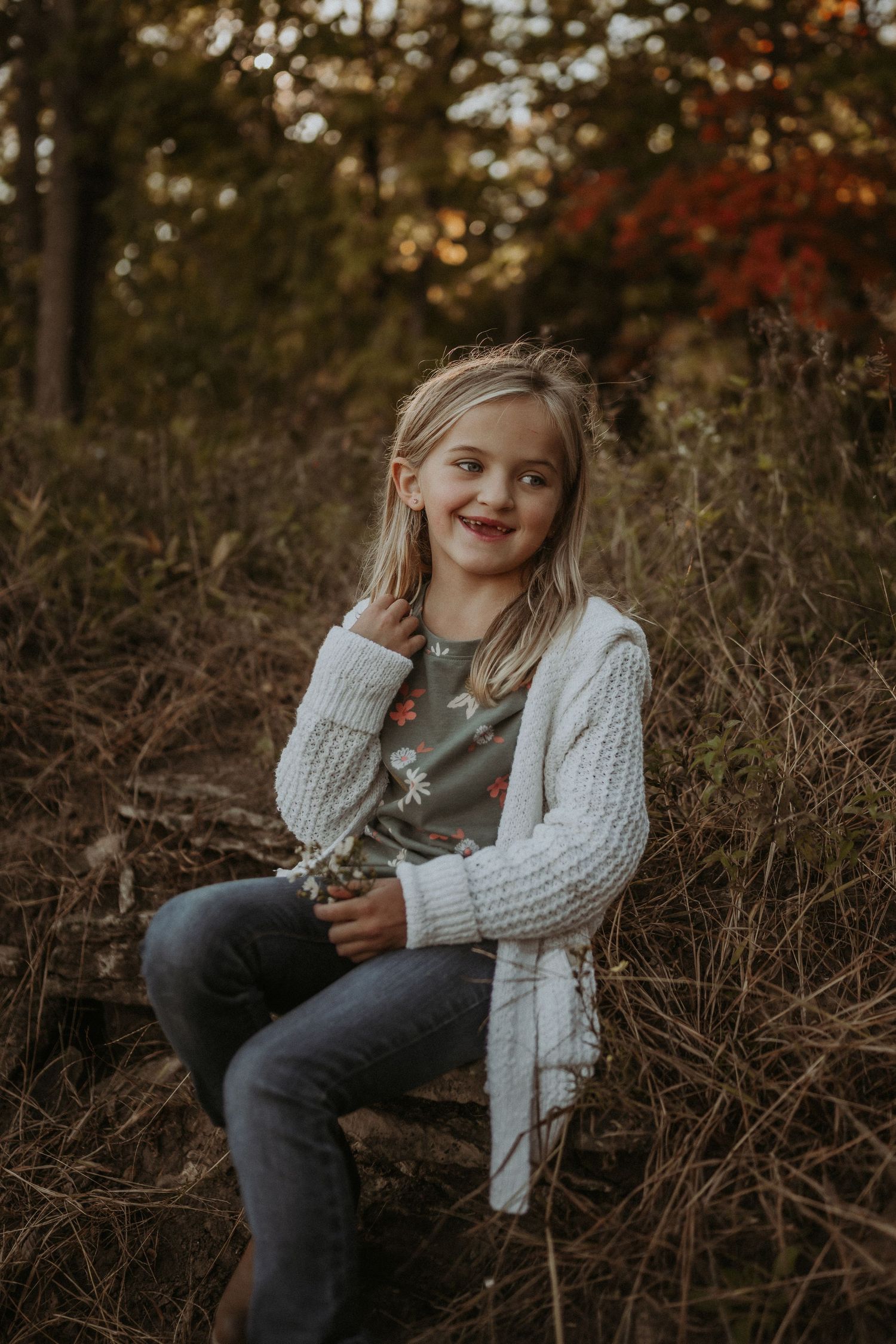 Natural outdoor portrait with white sweater against warm fall foliage background.