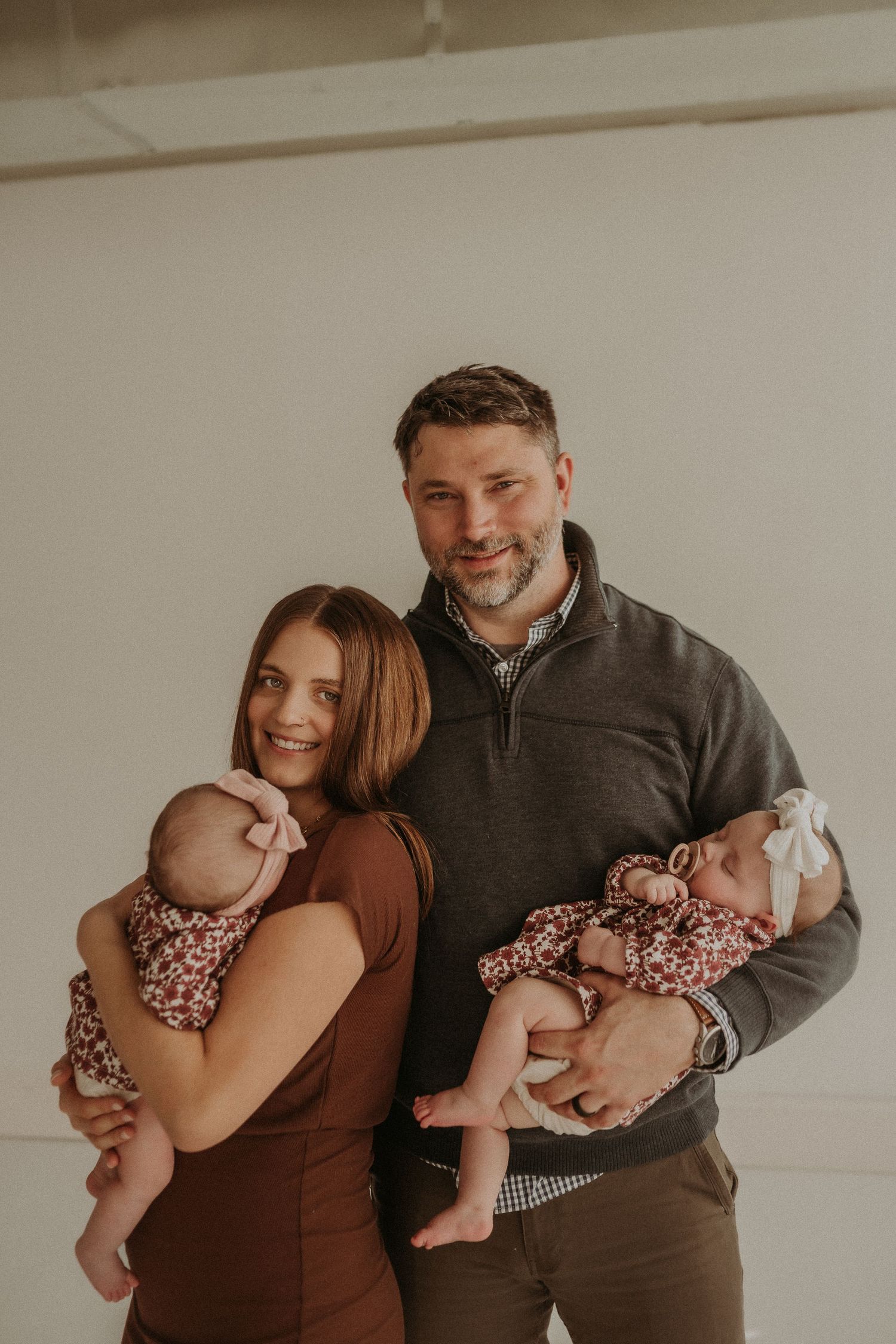 Parents hold twin babies wearing matching floral outfits in a bright studio setting.