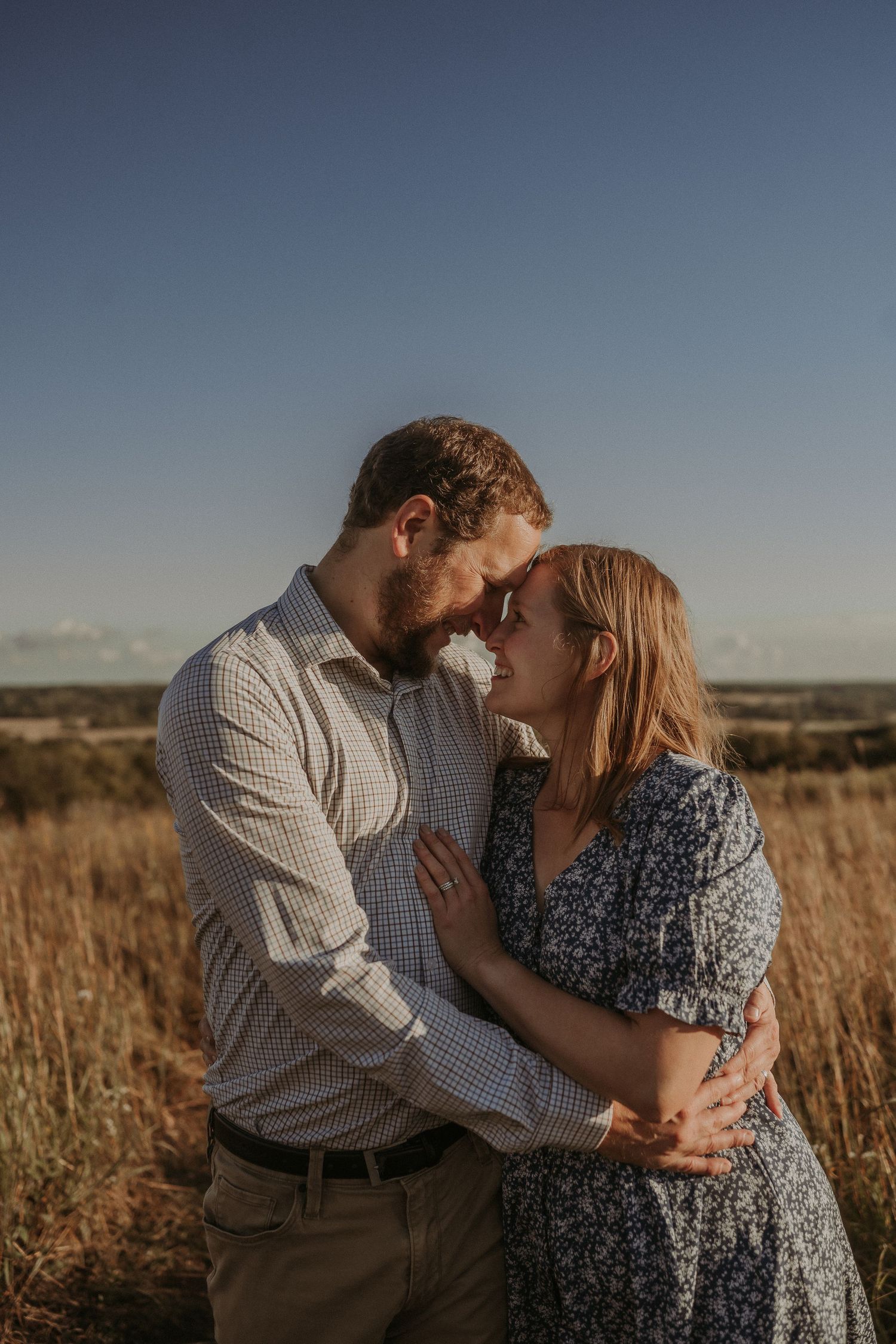 Intimate portrait of a couple embracing in a sunlit field during golden hour.