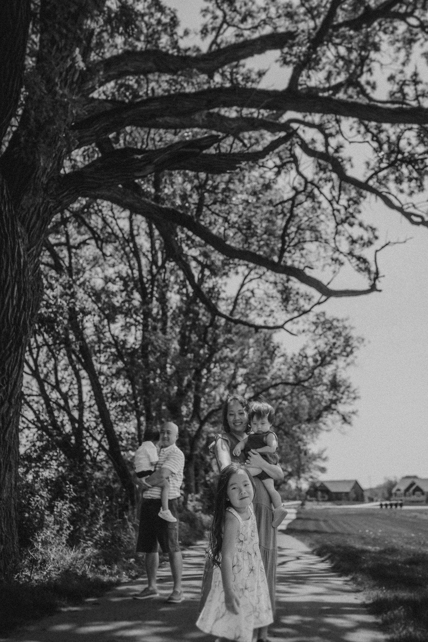 Black and white image of a family standing beneath sprawling tree branches on a rural path.