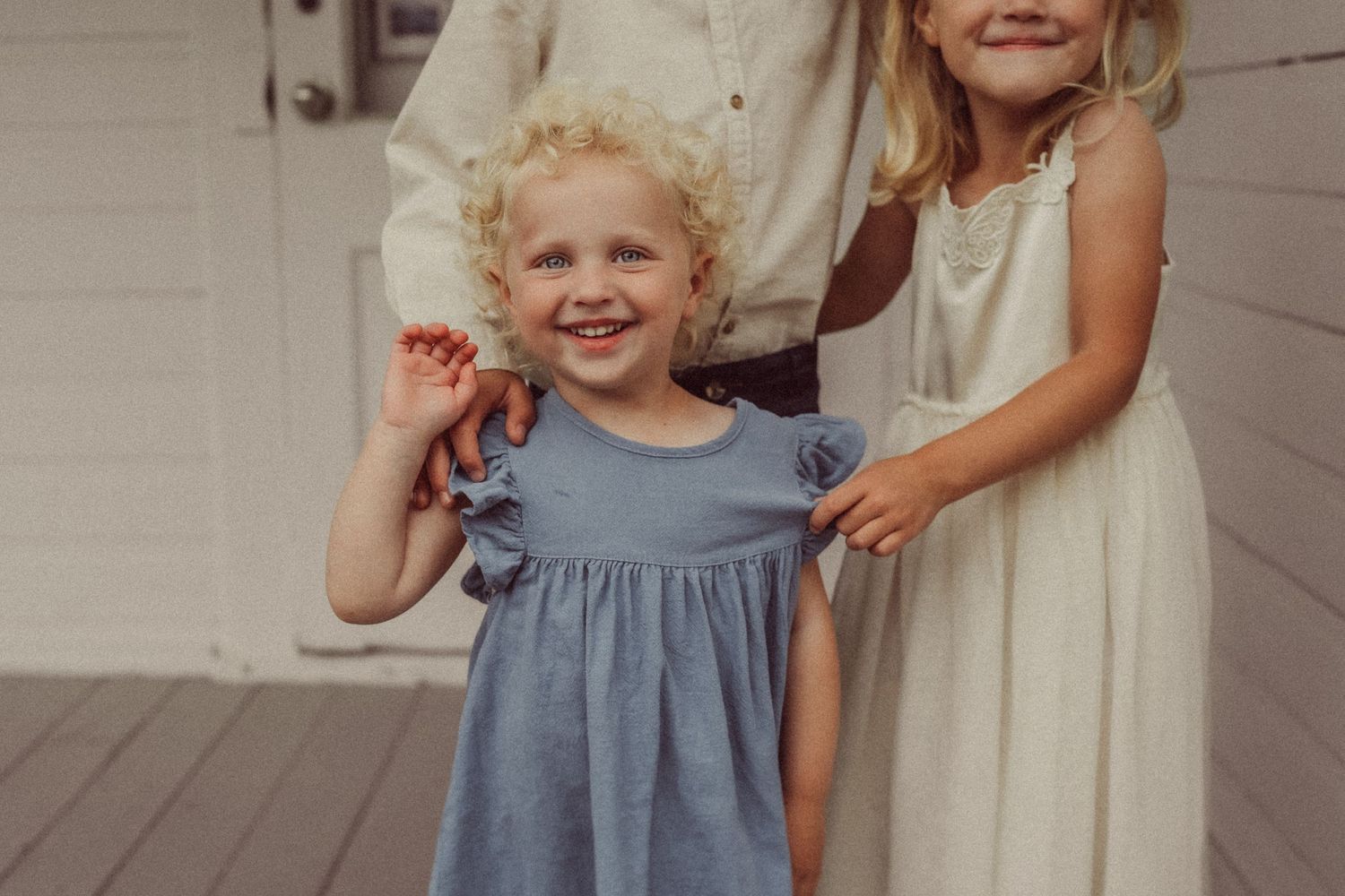 Close-up portrait on porch showing child in blue dress smiling joyfully.