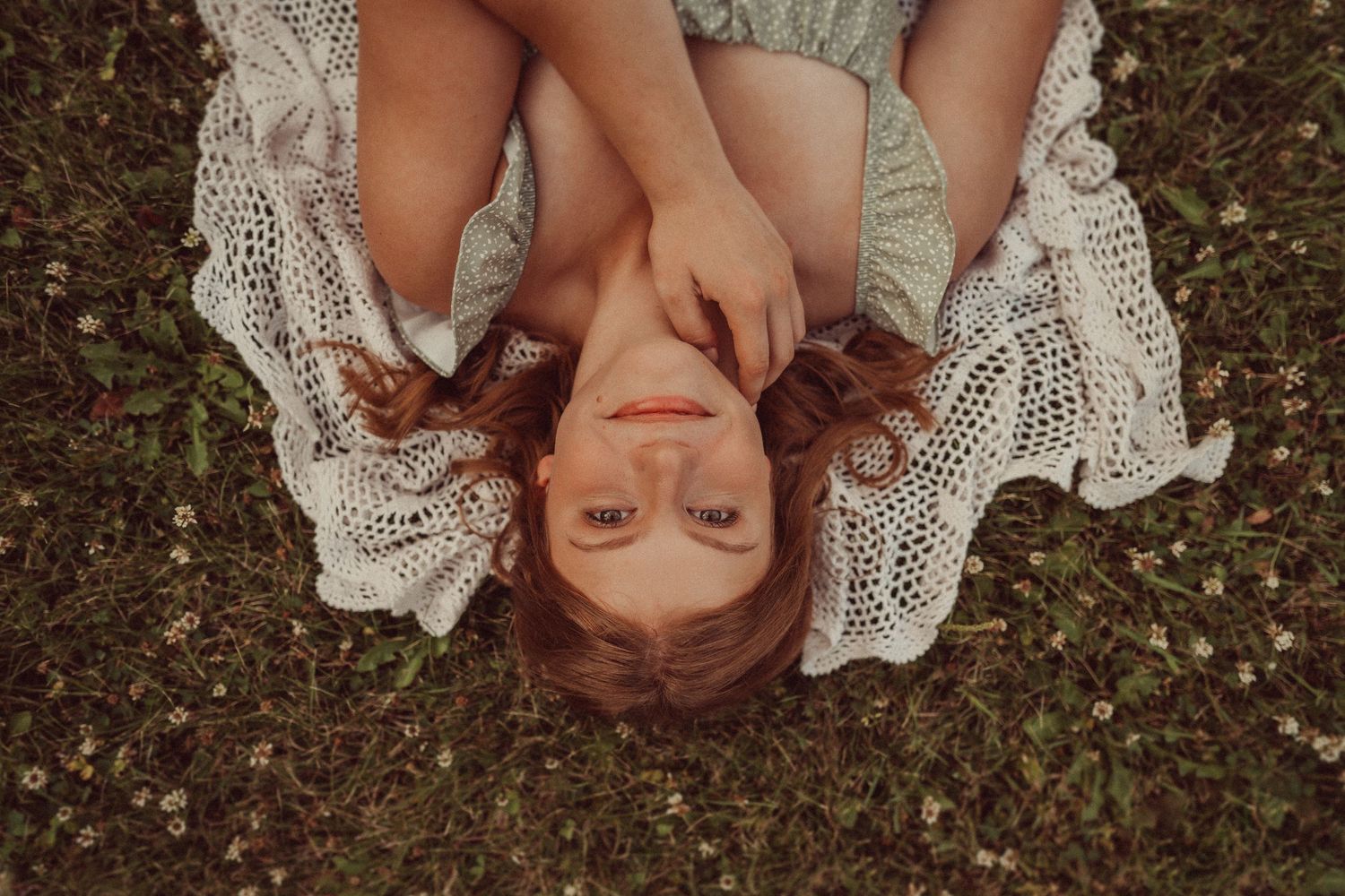 Overhead portrait of someone lying in white lace dress on grass with hair spread out.