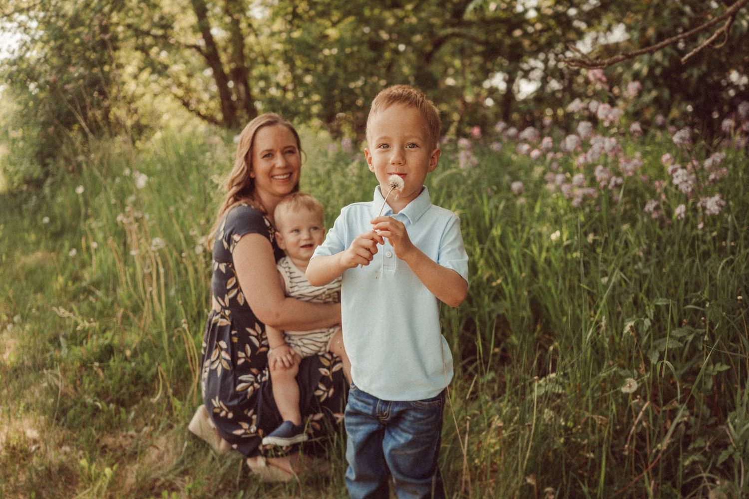 Family spending time together outdoors among tall grass and trees at sunset.