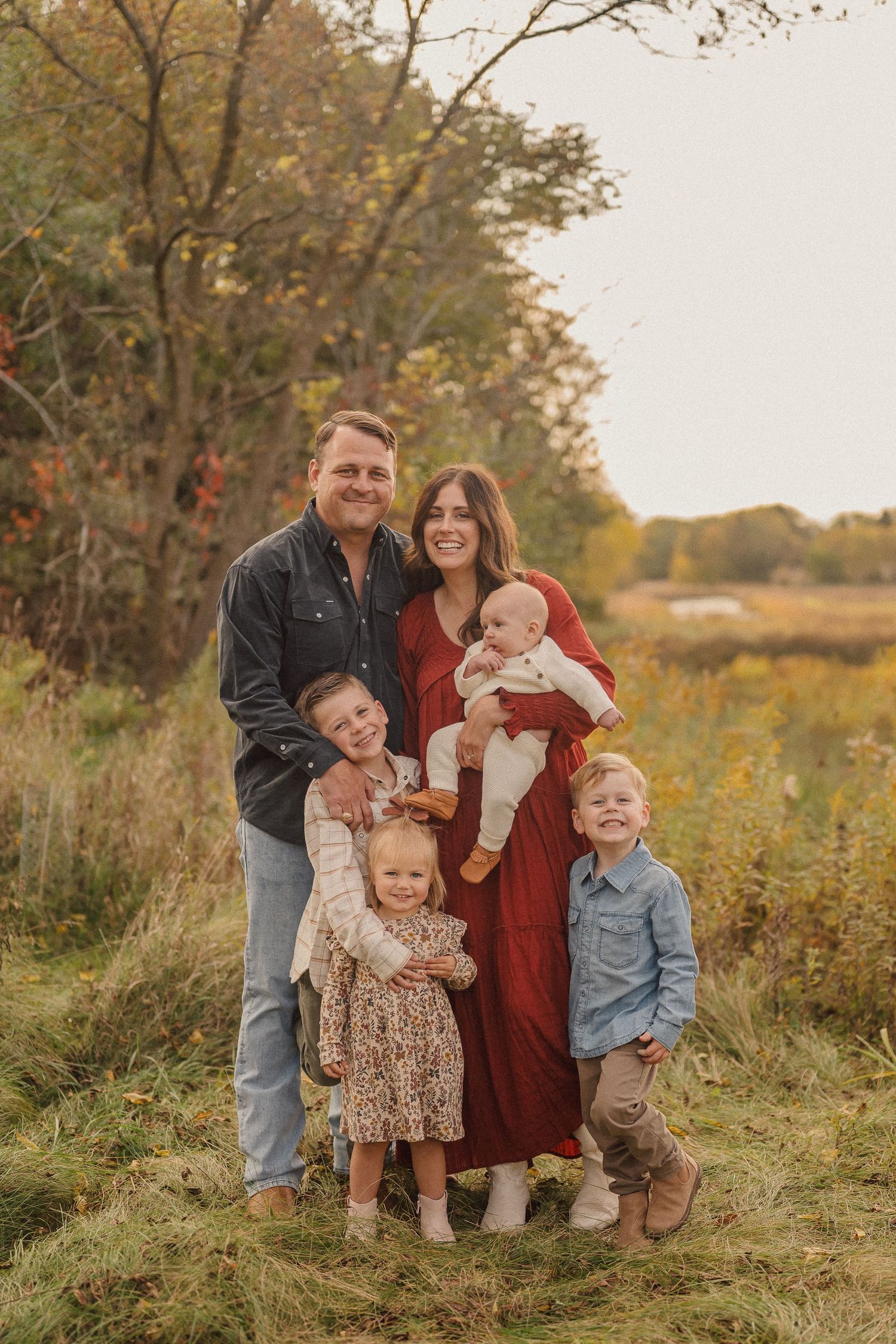 Casual outdoor family photo session in a meadow during golden hour with fall foliage.