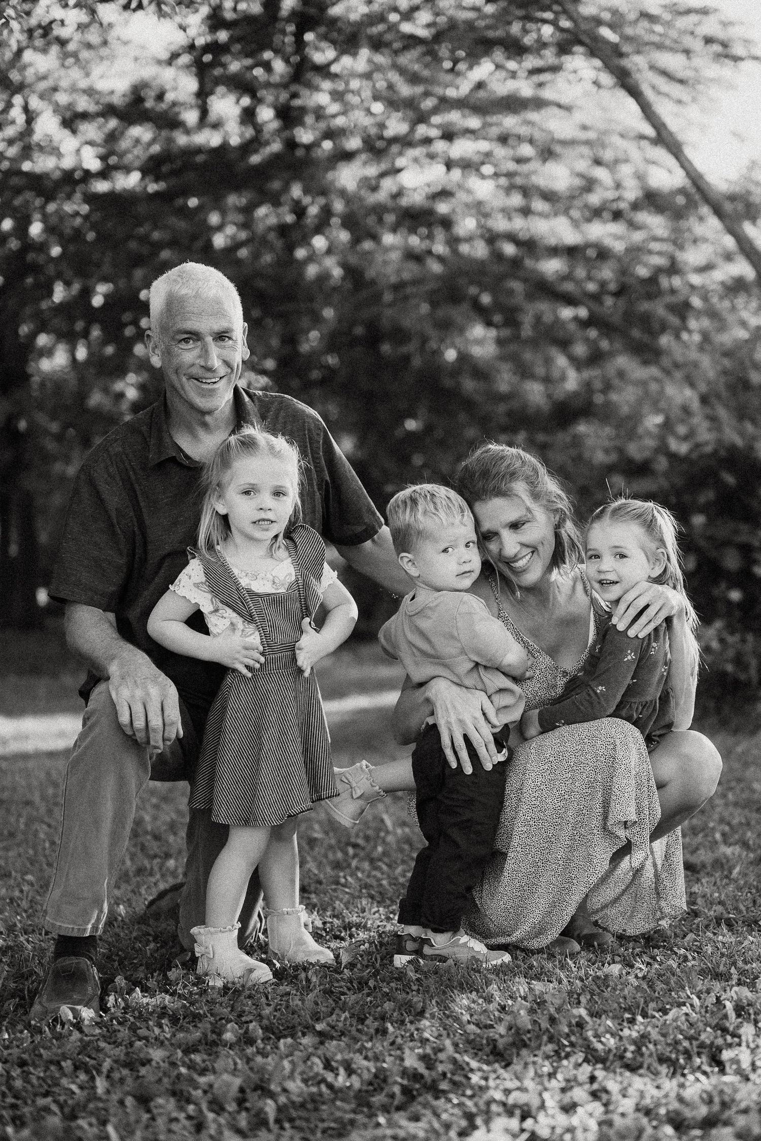Black and white family portrait of group sitting together on grassy hill in casual outdoor setting.
