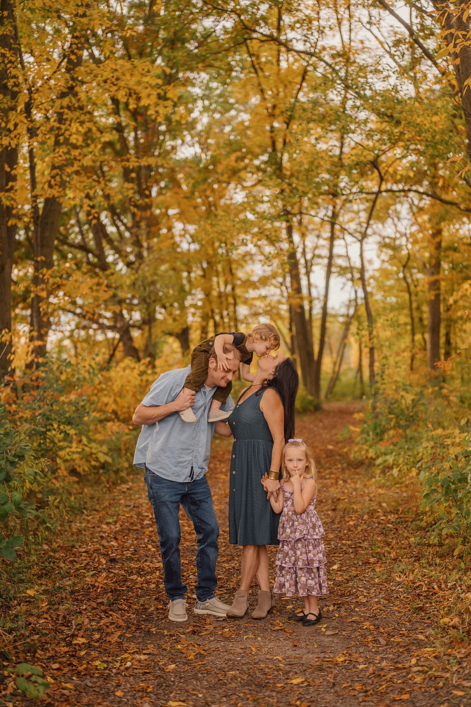 A family shares a joyful moment together on an autumn trail surrounded by golden trees.
