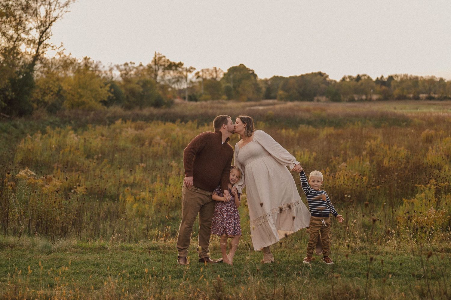 People dance and play together in a grassy meadow at golden hour with long shadows cast across the field.