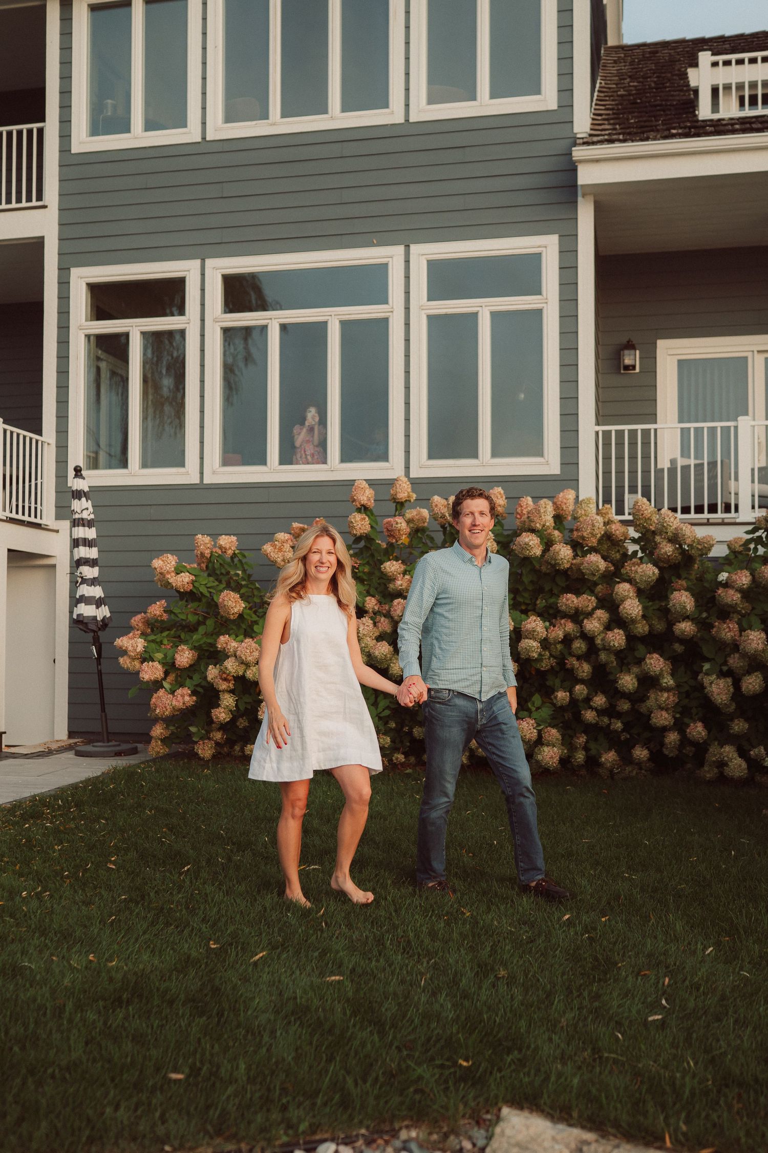 Family portraits taken on a sloping lawn with beautiful hydrangea bushes against a gray house exterior.
