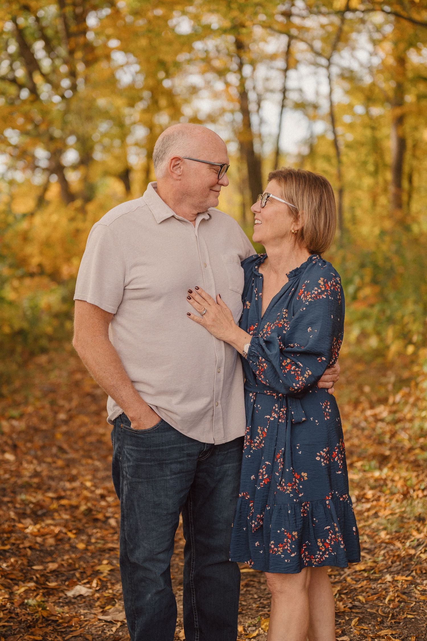 A couple shares a tender moment surrounded by golden autumn foliage in a forest setting.