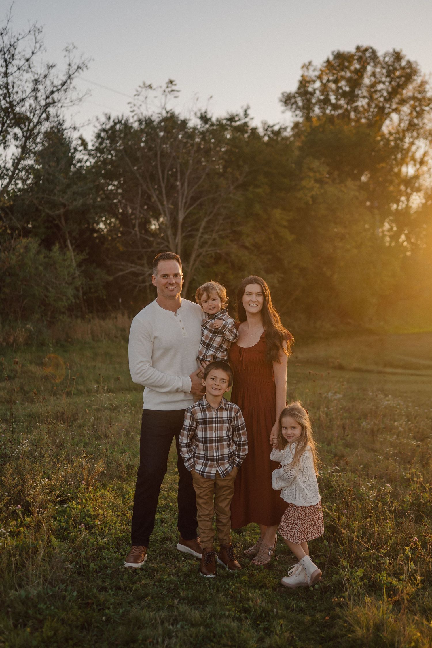 A group poses together in a golden sunset field with wildflowers and trees in the background.