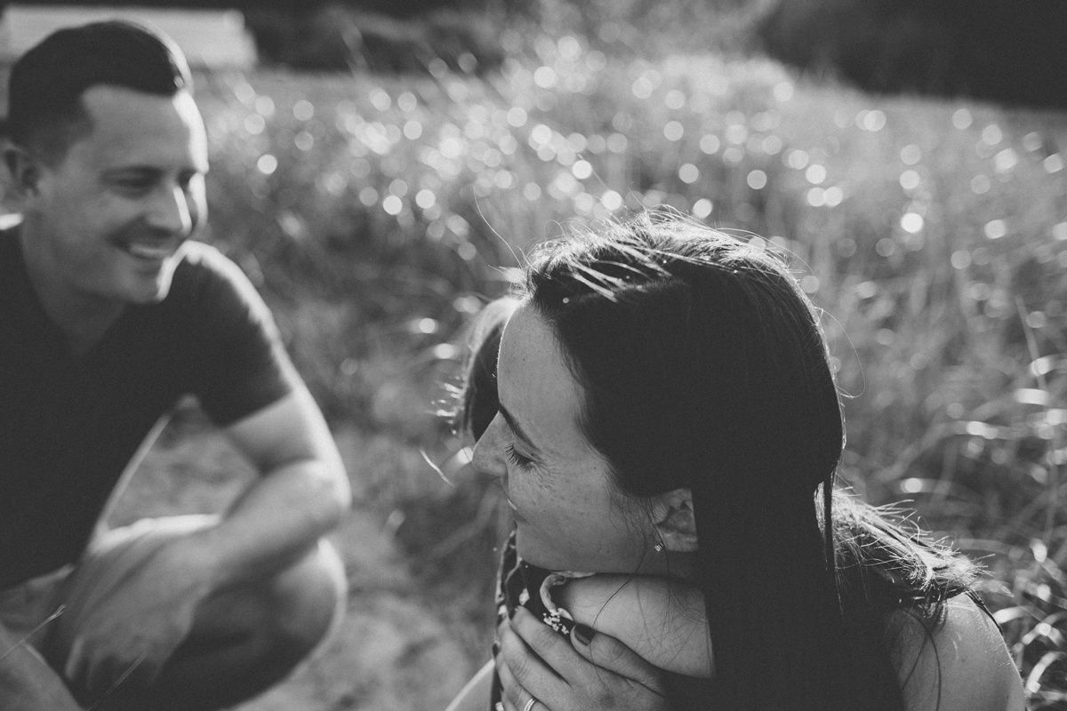 A candid black and white photo of a couple sharing a joyful moment in a sunlit meadow.