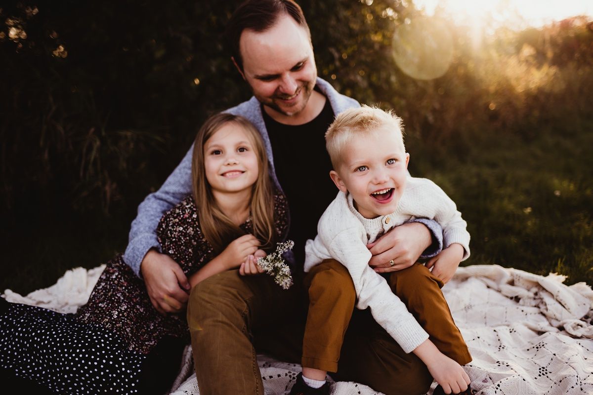 Family sharing joyful moment together on blanket during sunset photo session.