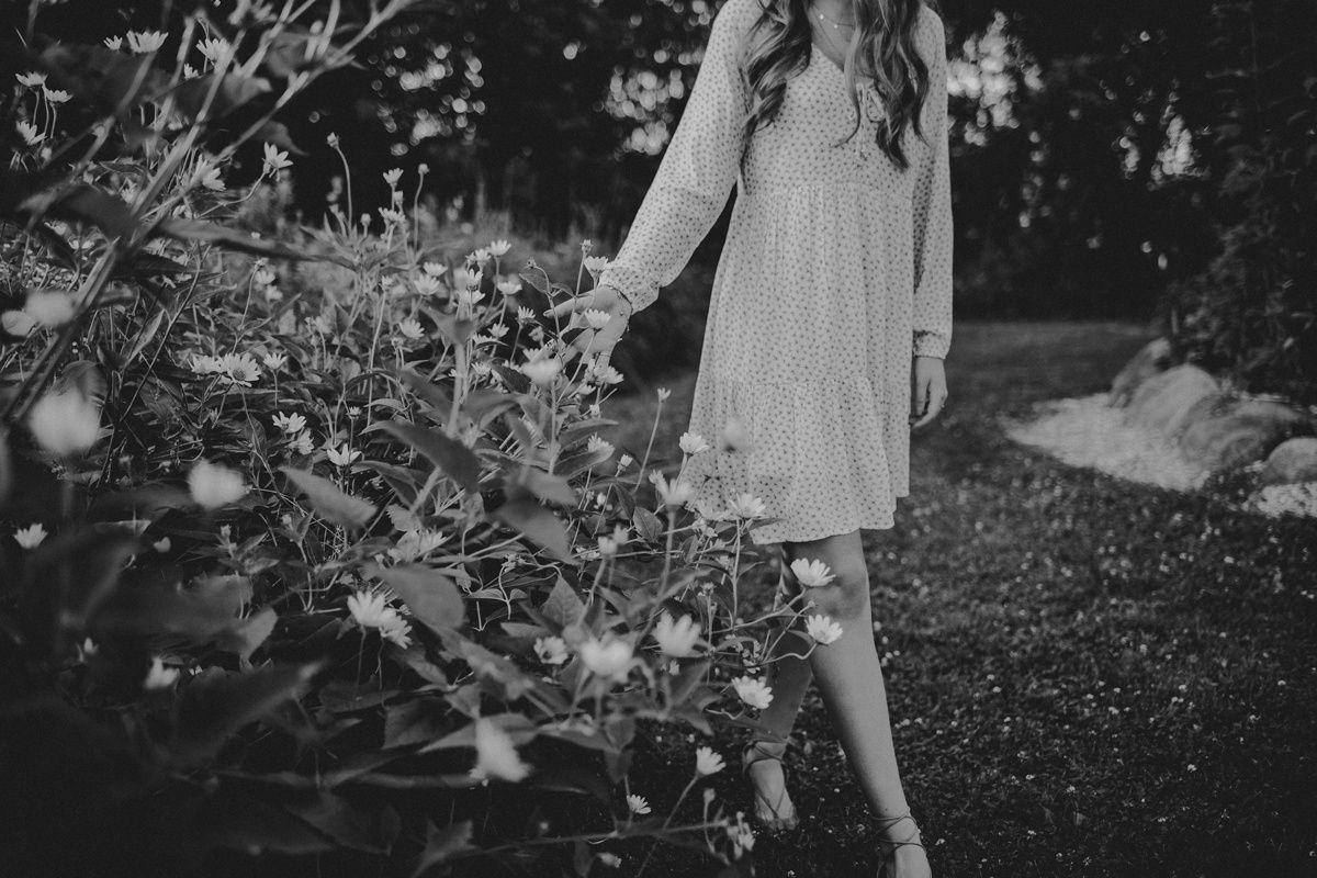 Black and white photo of figure in light dress standing beside garden flowers.