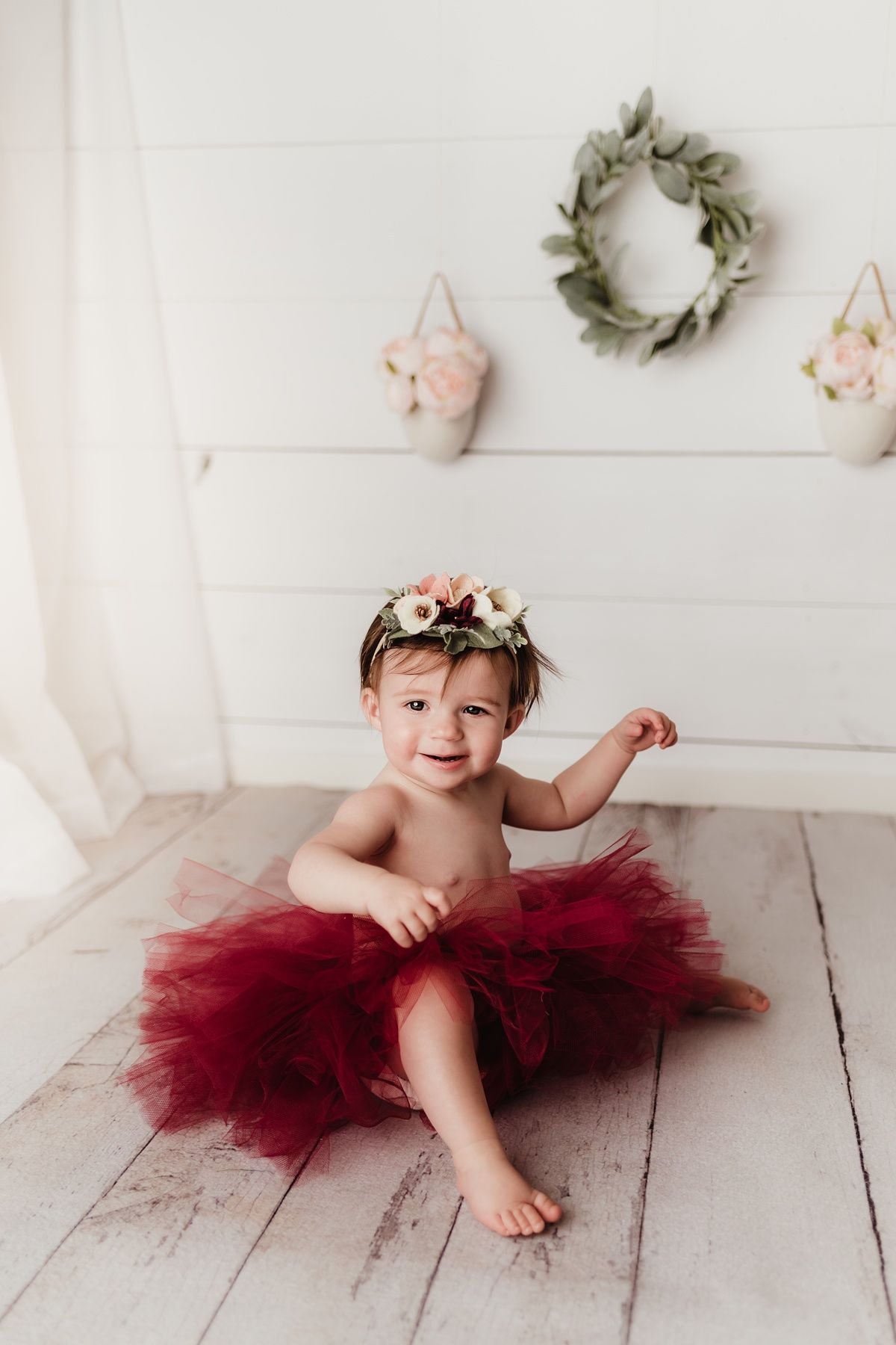 Festive birthday photo with red tulle tutu and floral crown against white shiplap wall.