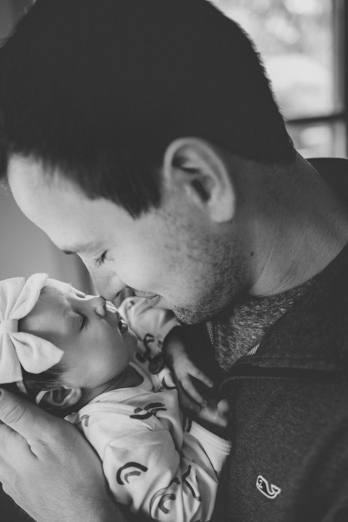 Black and white intimate moment of parent leaning in close to newborn.