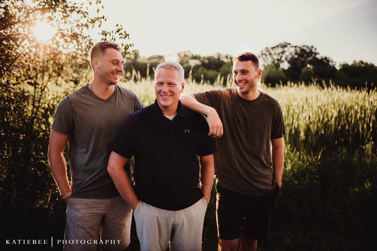 Three people standing together outdoors during golden hour with trees in the background.