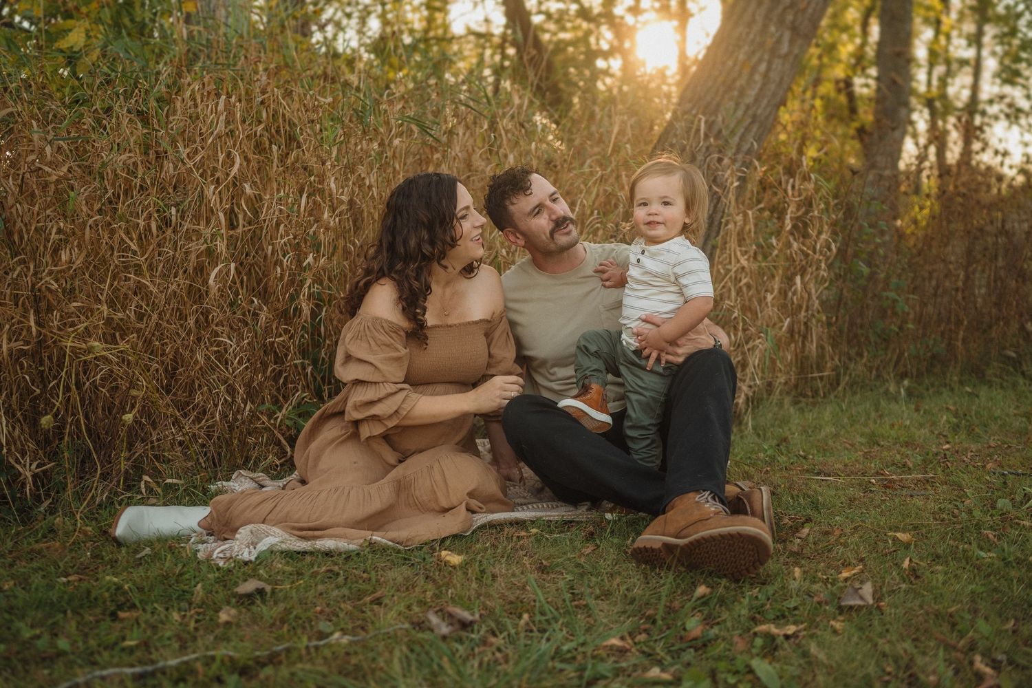 A family shares intimate moments while sitting on a blanket surrounded by autumn grasses at sunset.